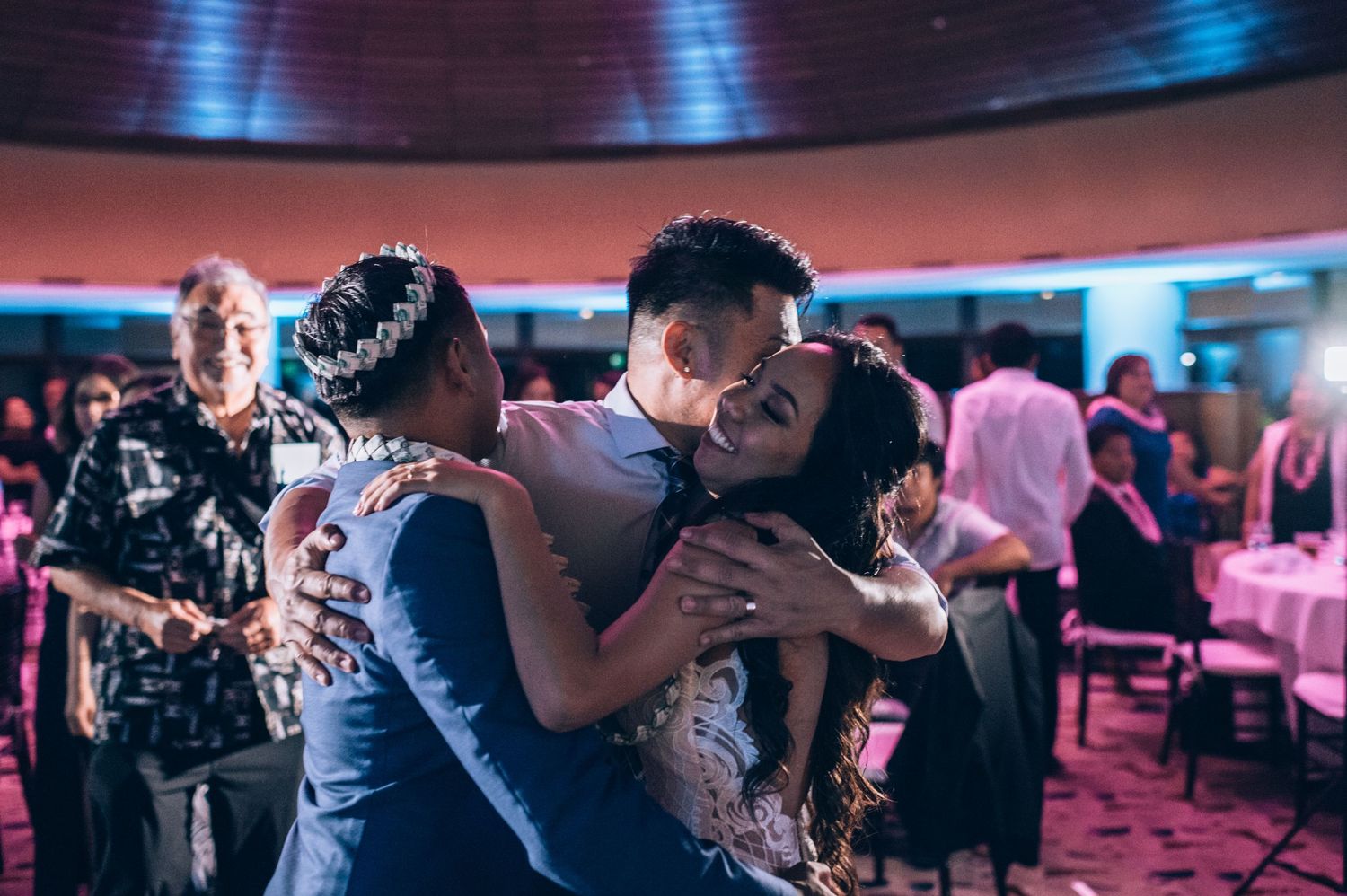 Wedding guests dance together in an intimate ballroom setting with dramatic blue lighting.