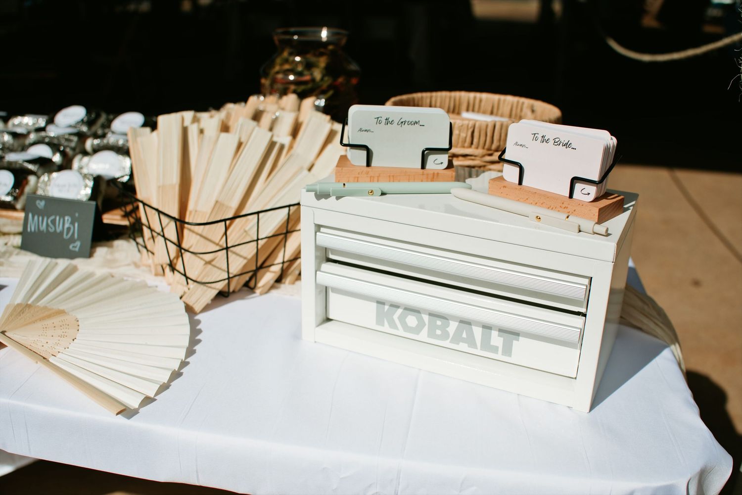 Hand fans and cards arranged on a white wedding reception table.