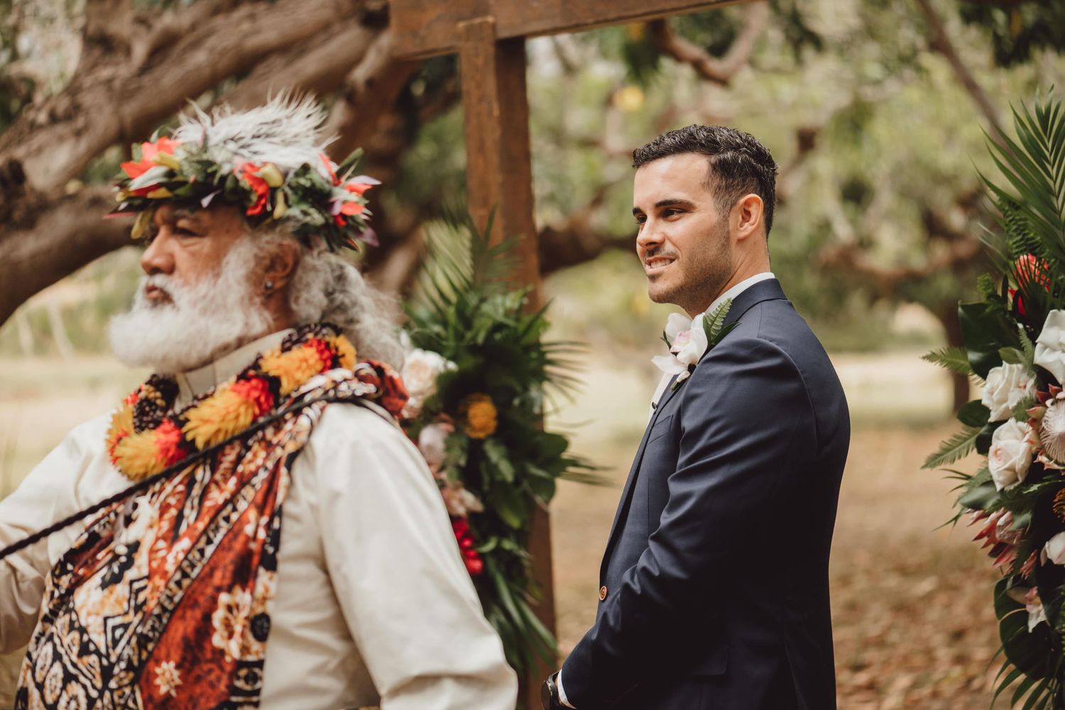 Outdoor wedding ceremony setup with floral arrangements and wooden arch under tropical trees.