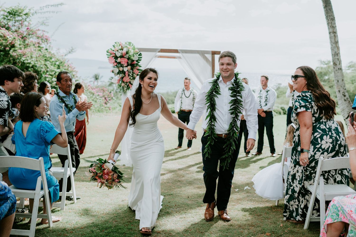 Wedding celebration on a grassy lawn with palm trees and ocean views.