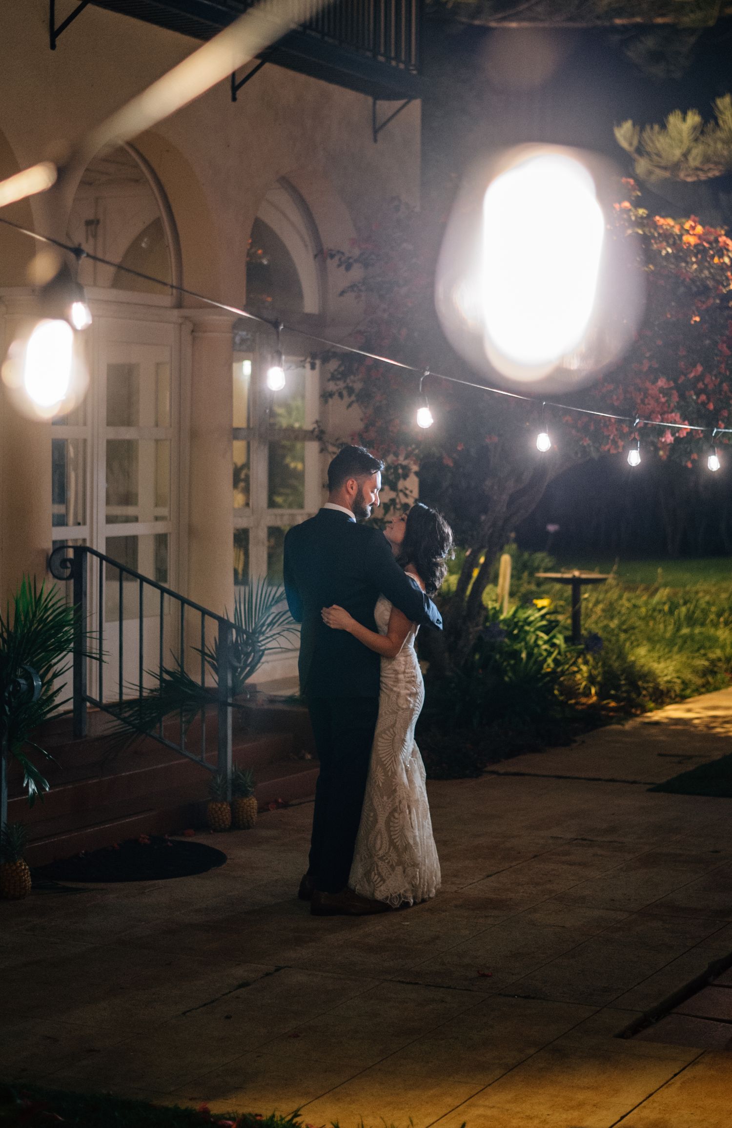 Romantic evening dance under string lights at an elegant venue with arched architecture.
