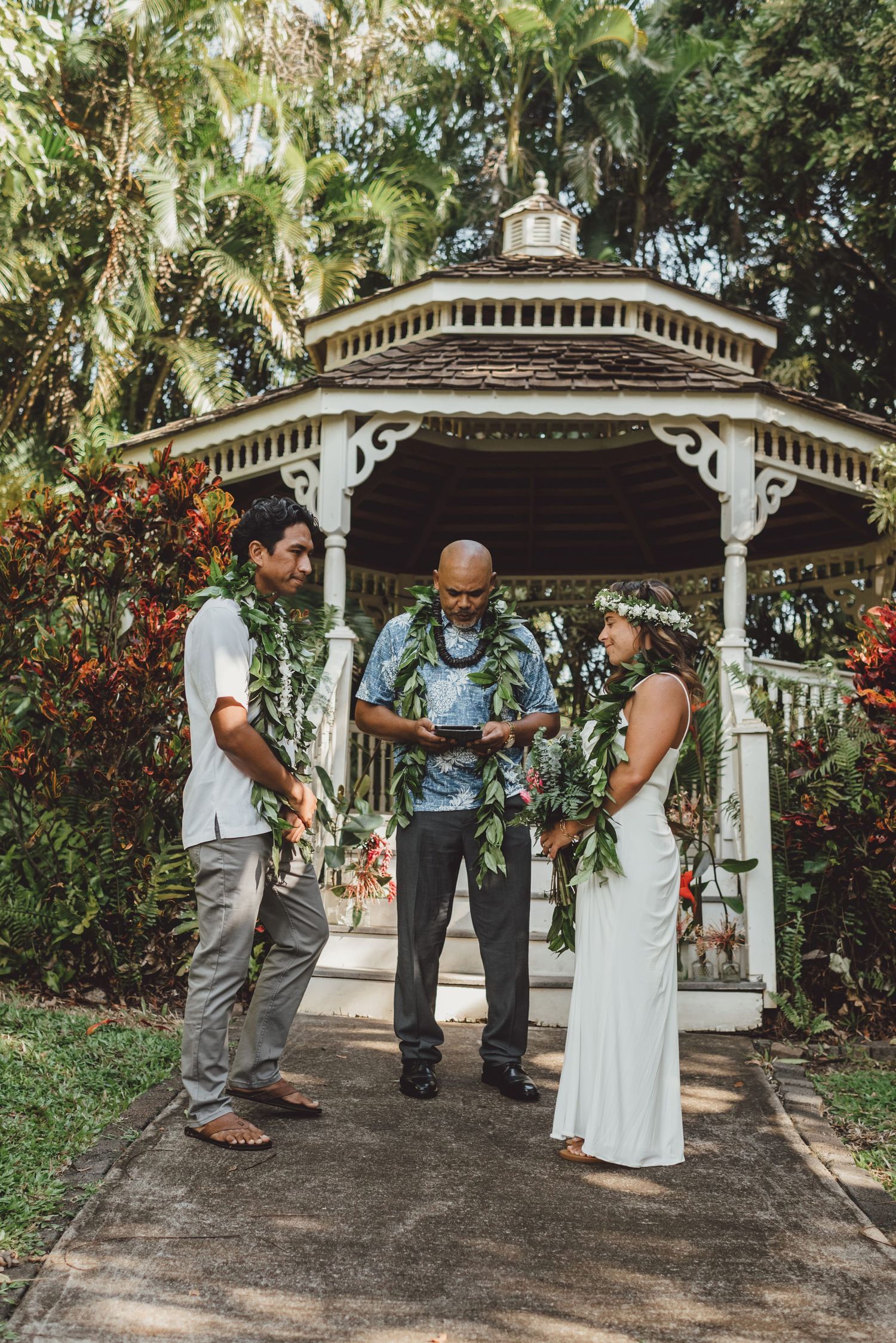 Couple exchanges vows at a gazebo wedding ceremony in Hawaii, wearing traditional lei garlands with an officiant.