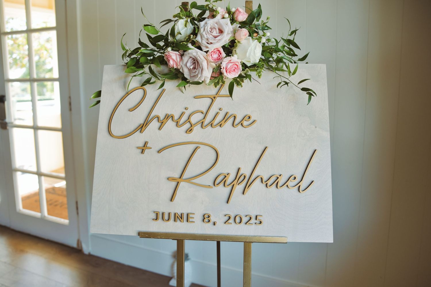 Wedding welcome sign reading Christine and Raphael June 8 2025 decorated with pink and white flowers.