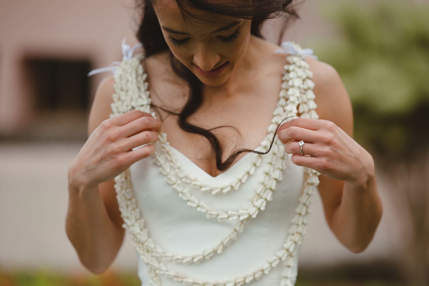 Bride adjusting her white floral lei necklace on a elegant wedding dress outdoors.