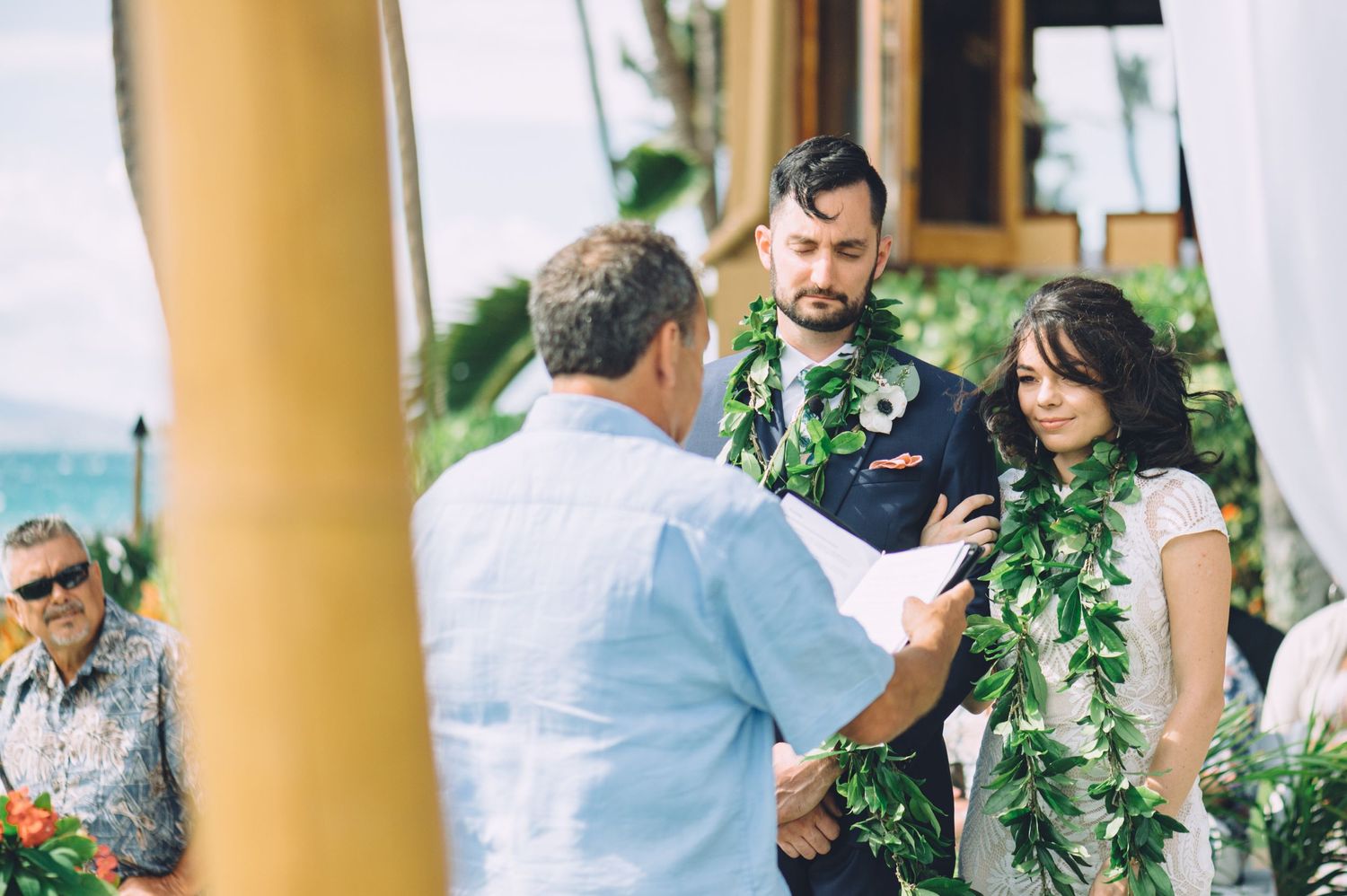 Outdoor wedding celebration with guests mingling near tropical pillars.