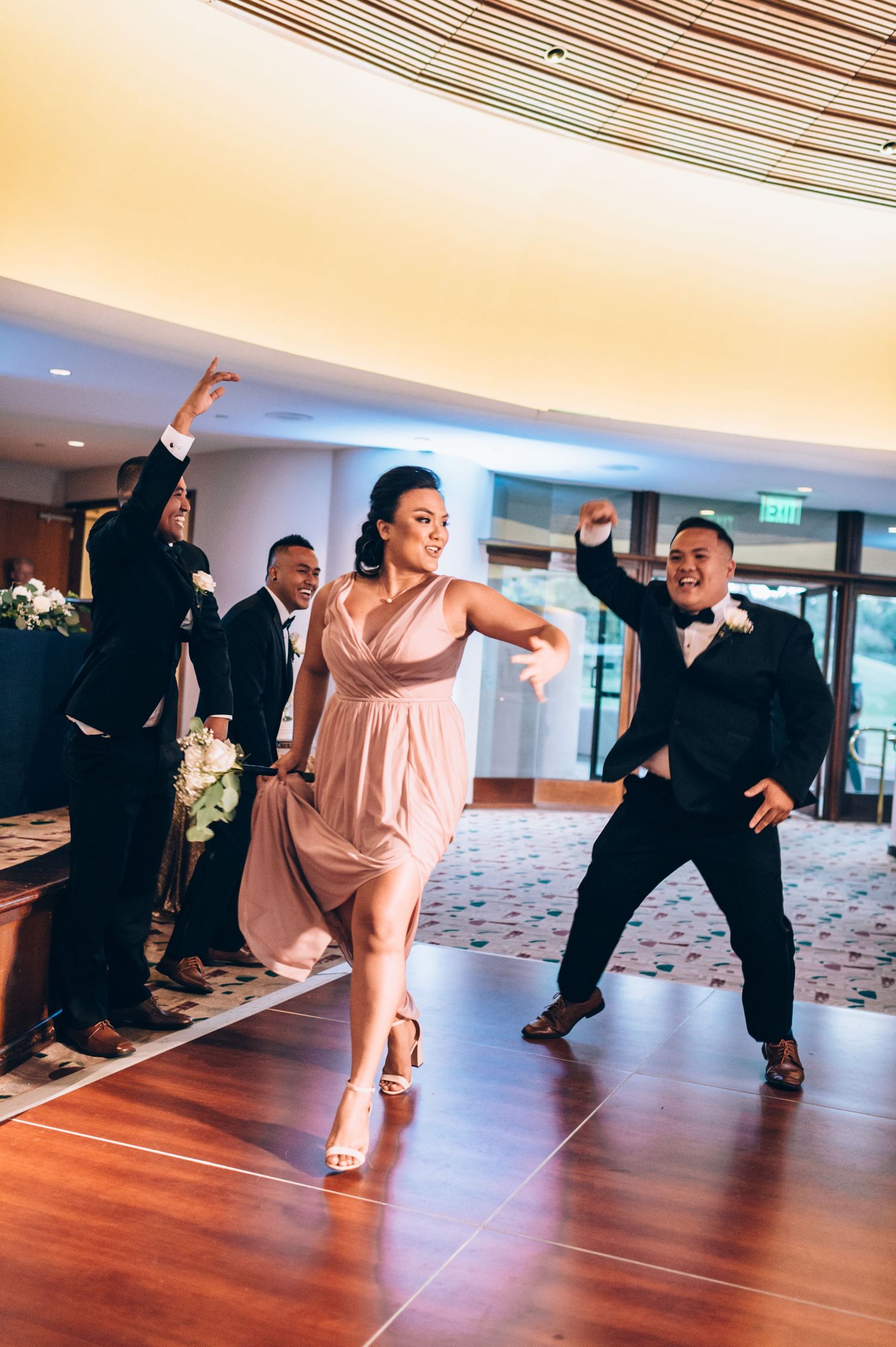 Wedding party members strike dynamic poses during choreographed dance performance on wooden floor.