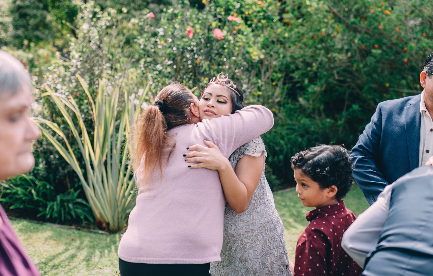 Guests mingle and embrace during a garden wedding celebration.