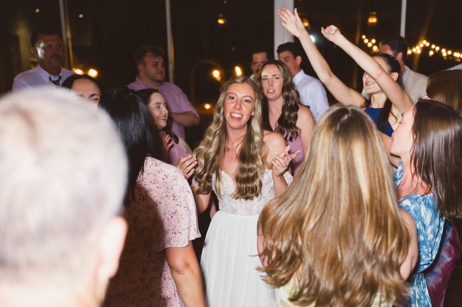 Bride in white gown dancing joyfully with guests at a lively wedding reception party.