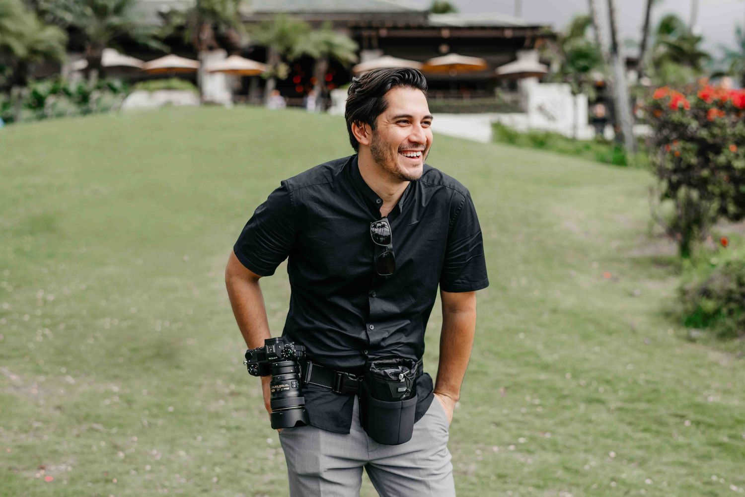 Professional wedding photographer smiling outdoors holding camera at tropical garden resort location.