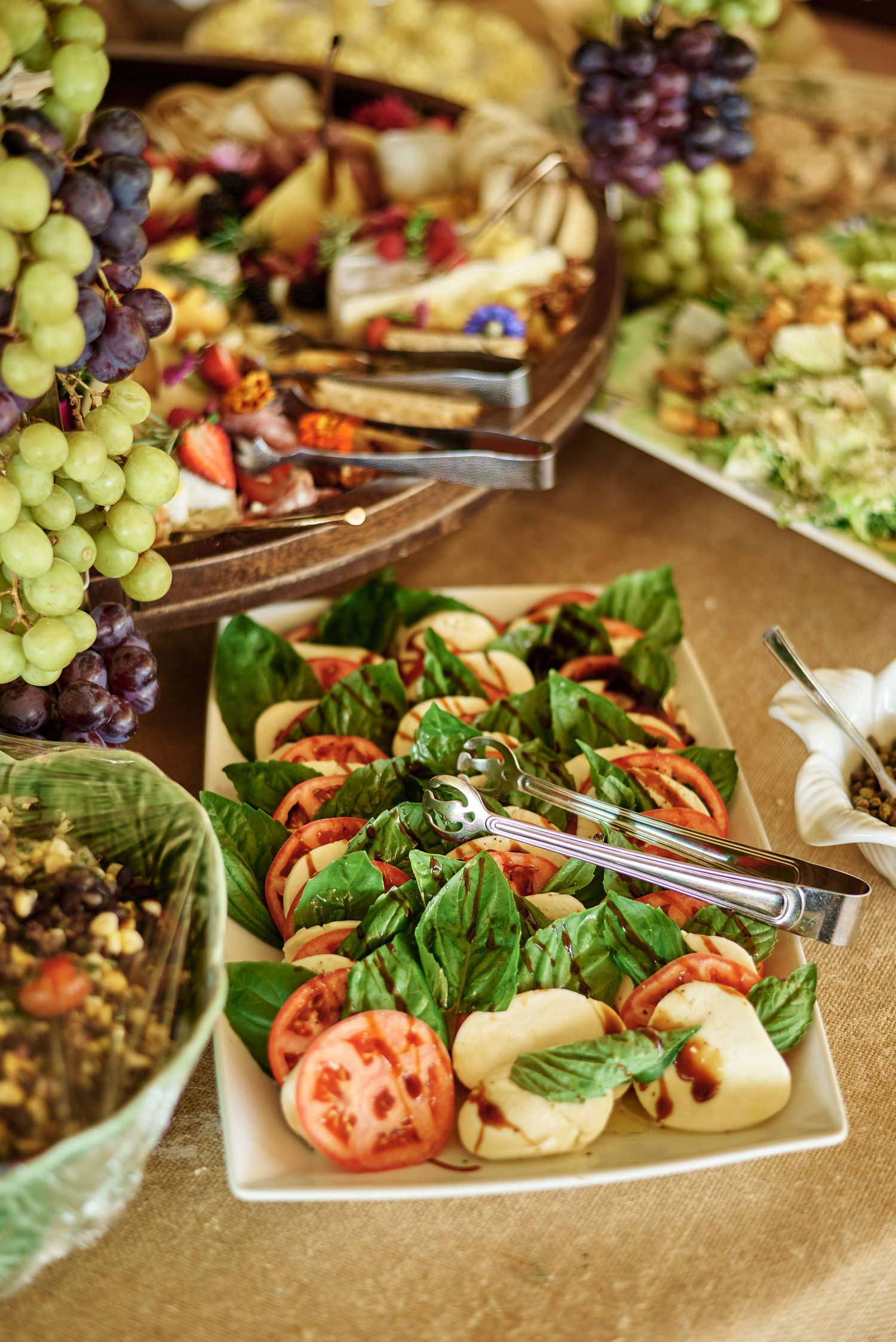 Fresh appetizer platter with grapes, tomatoes, salad greens and garnishes arranged on white plates.
