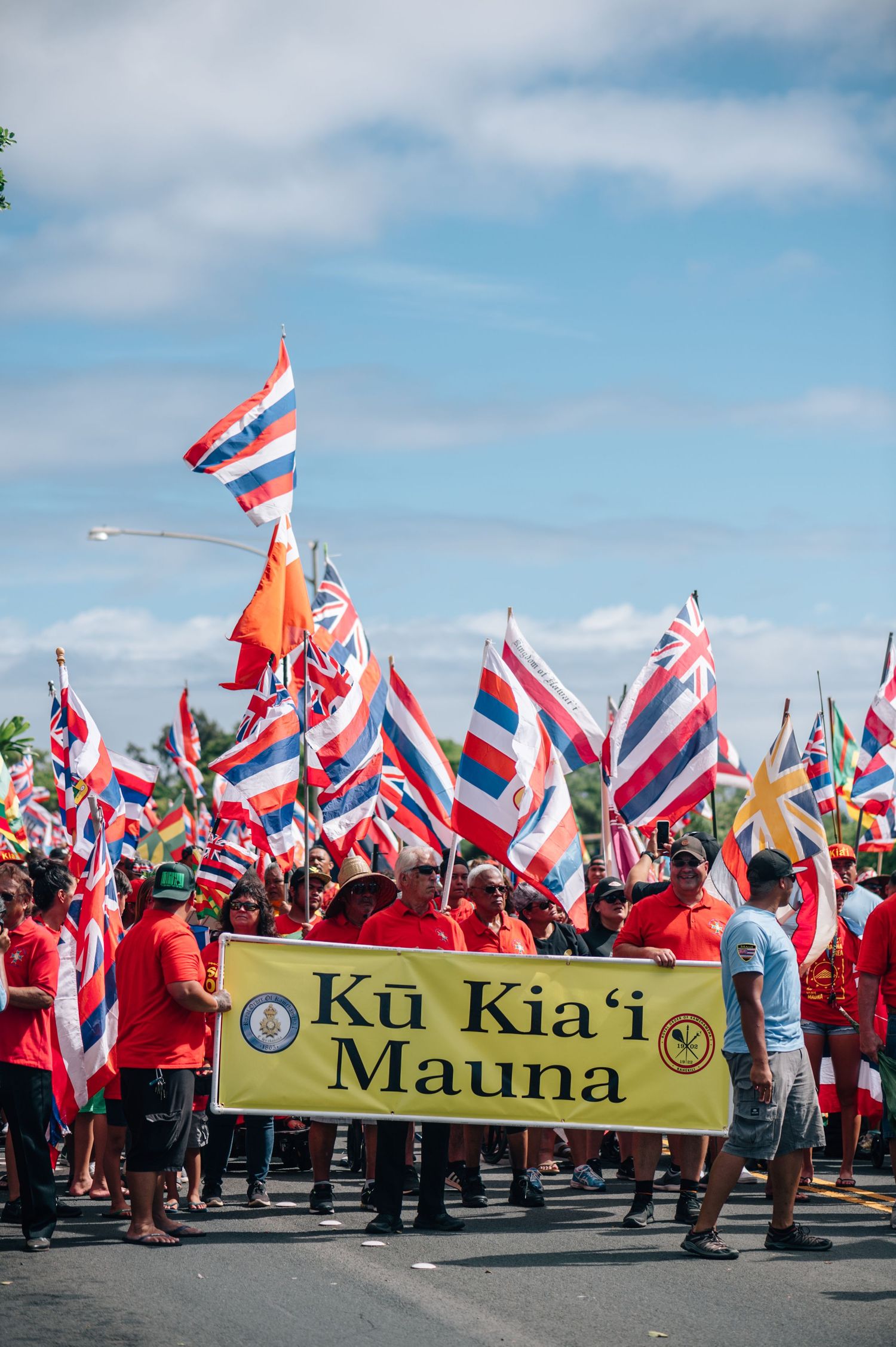 Demonstrators with Hawaiian flags gather around yellow Ku Kia'i Mauna banner.