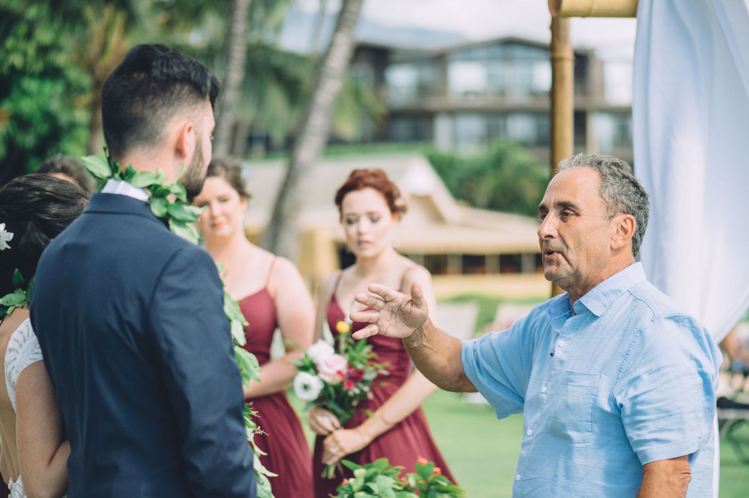 Wedding guests gather for a celebration on a tropical lawn with palm trees.