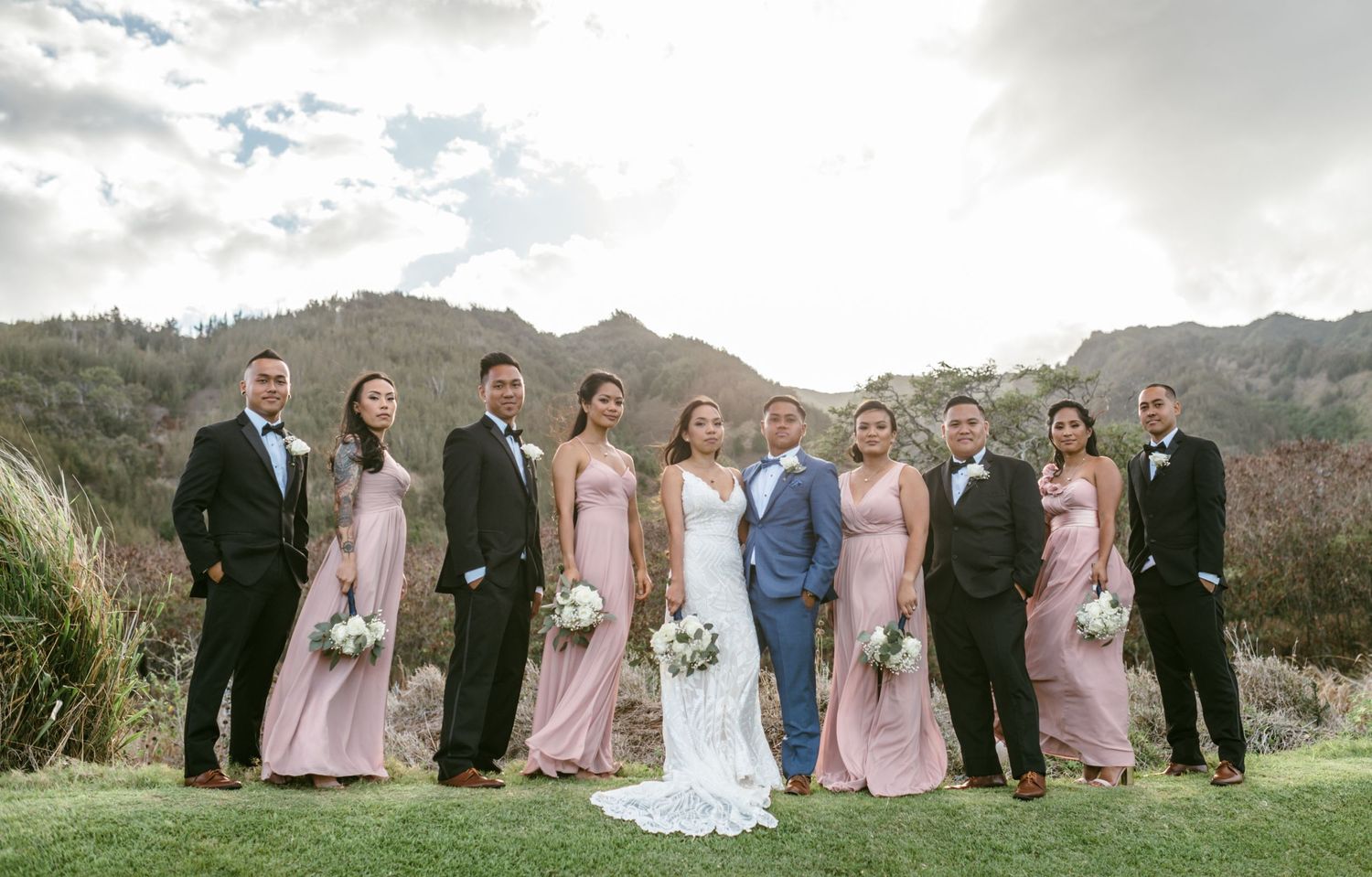 Wedding party poses for group photo on scenic mountain landscape.