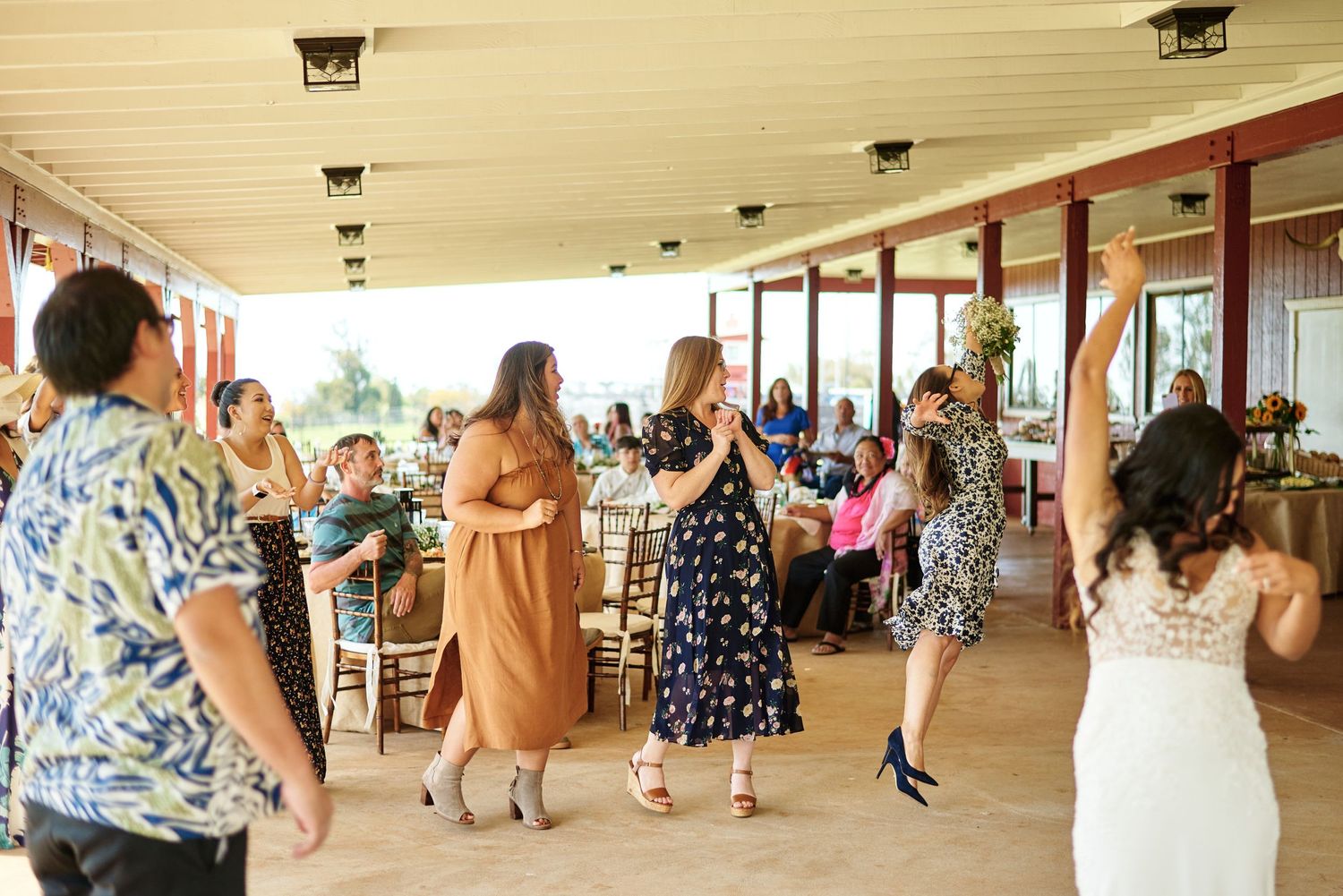 Wedding guests dancing and celebrating in covered outdoor venue with wooden beams.
