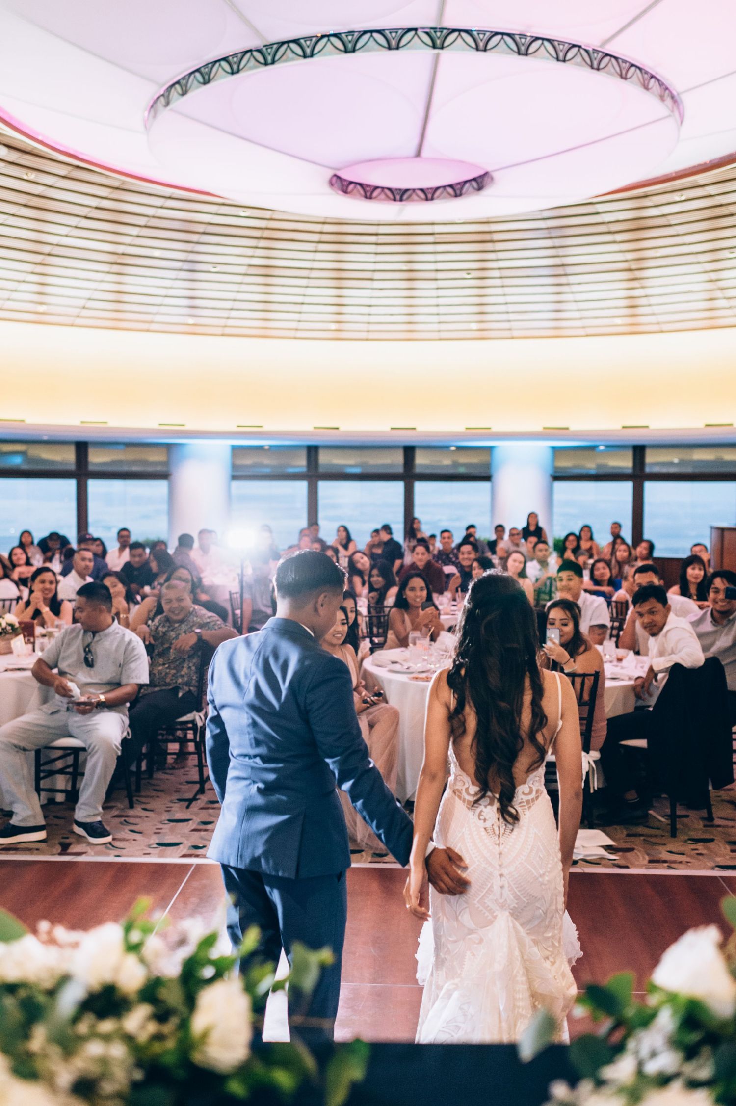 Wedding reception dance floor filled with guests under elegant ceiling lighting.