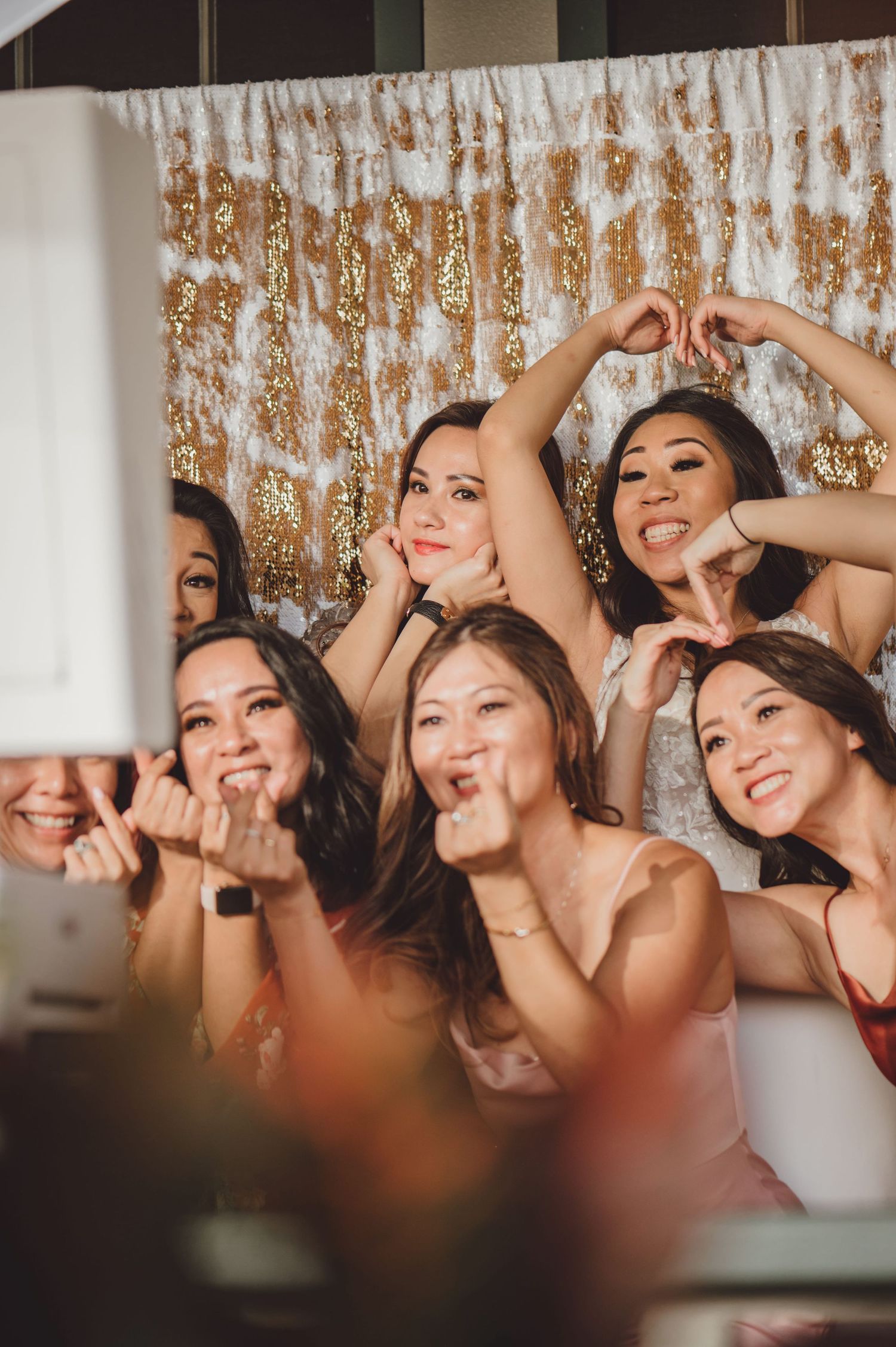 Group of women posing and making fun gestures in front of a gold sequin backdrop at a celebration.