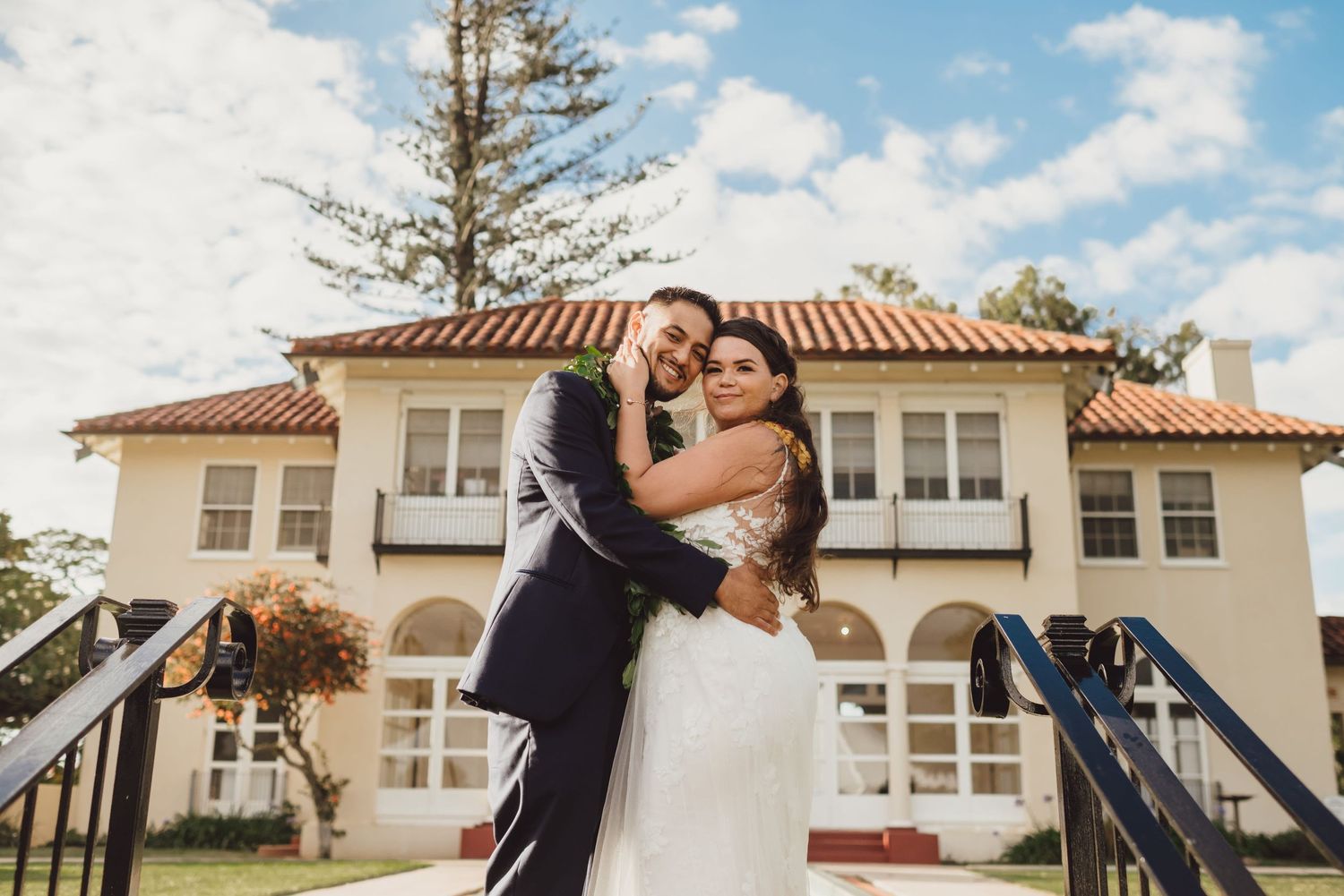Newlywed couple embracing in front of elegant Spanish-style villa on their wedding day.