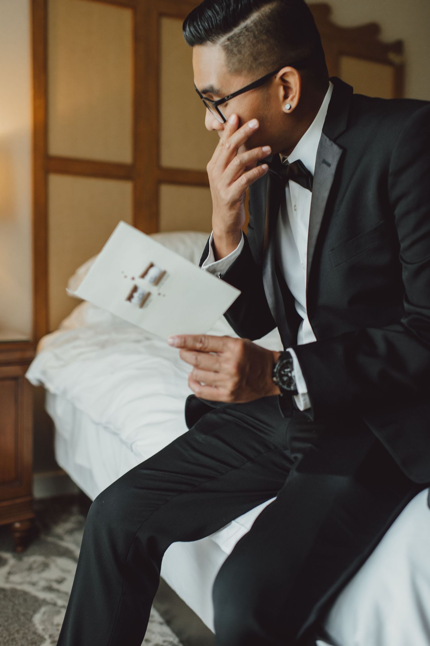 Emotional wedding moment as groom reads letter in formal black suit and glasses.