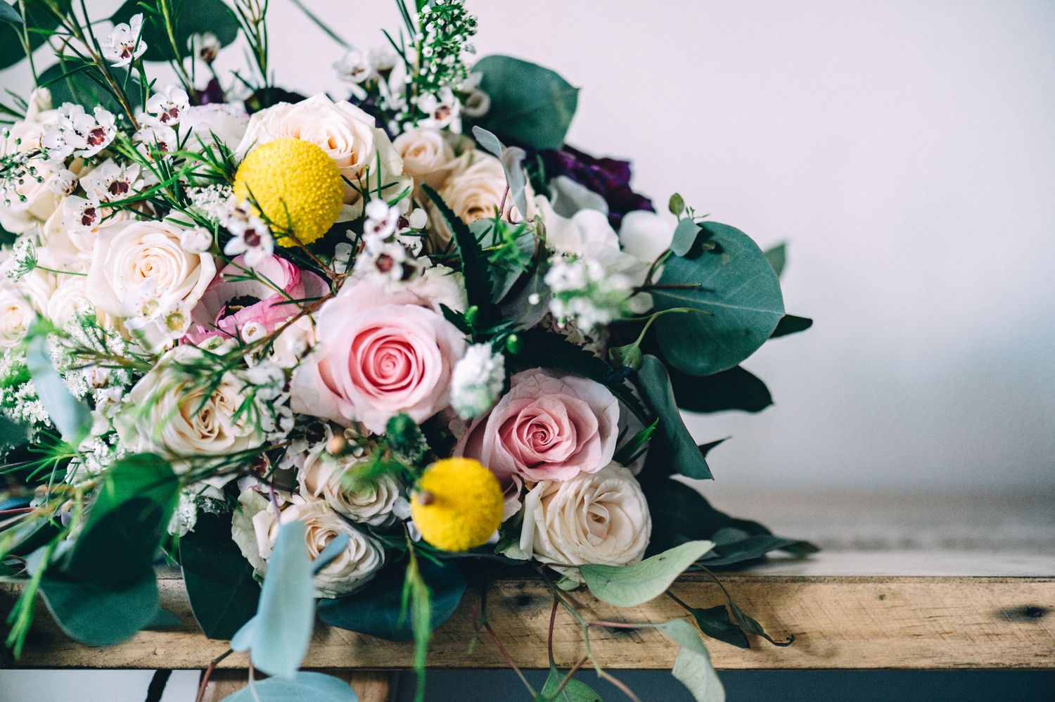 Romantic wedding bouquet with pink roses, yellow lemons, and eucalyptus on wooden surface.