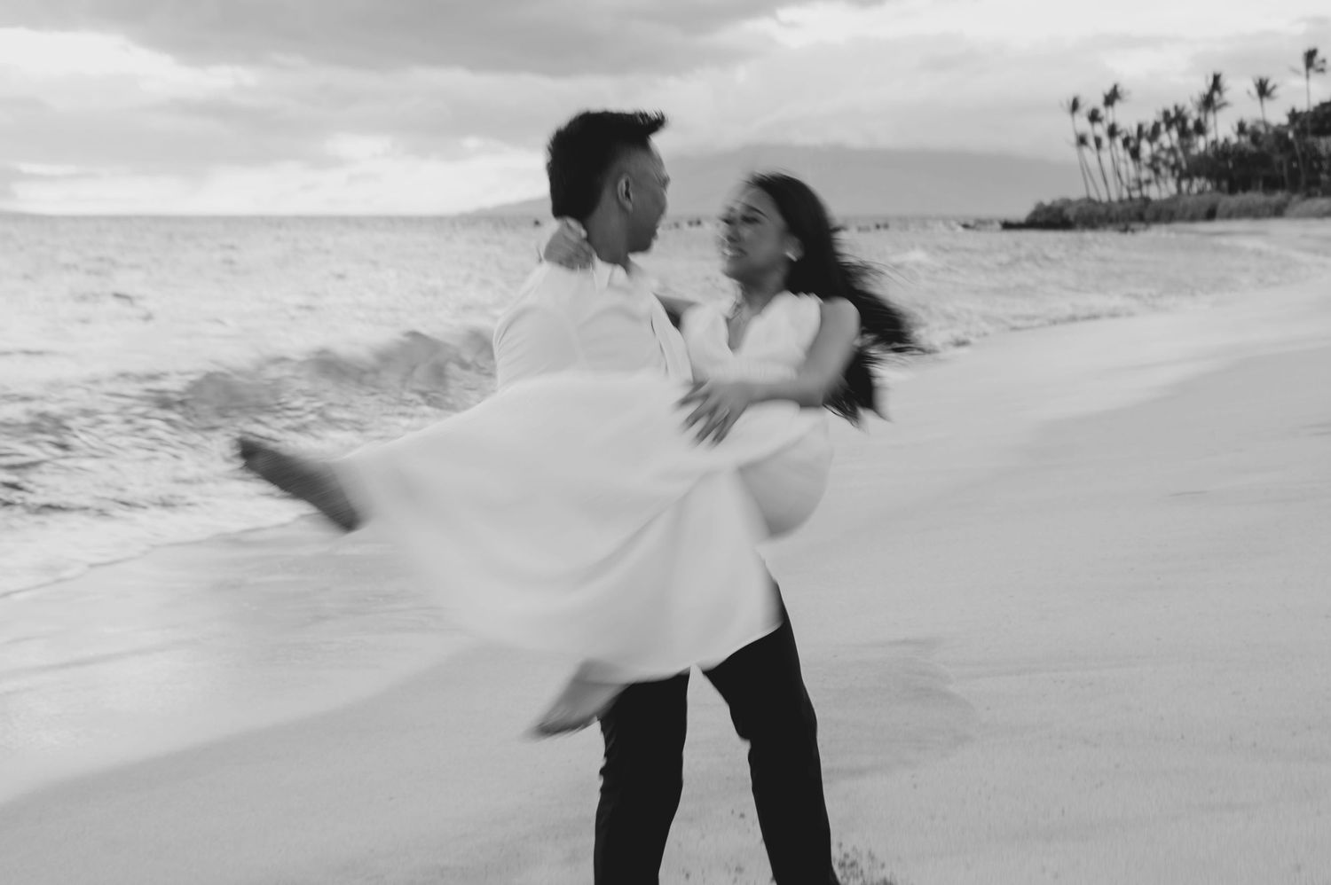 Couple dancing joyfully on beach shore in black and white motion blur photo.