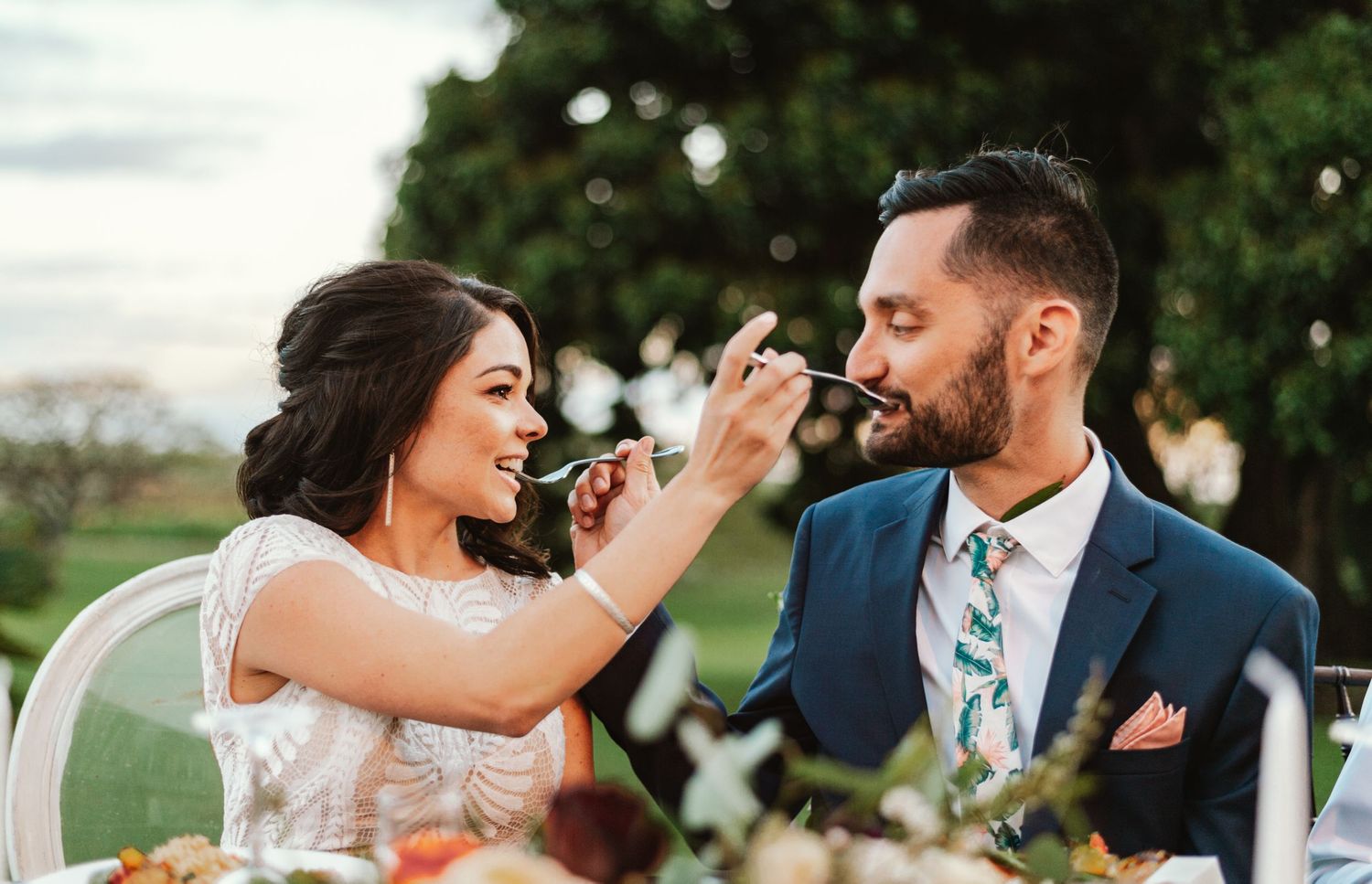 Playful moment of newlyweds feeding each other during their outdoor wedding reception.