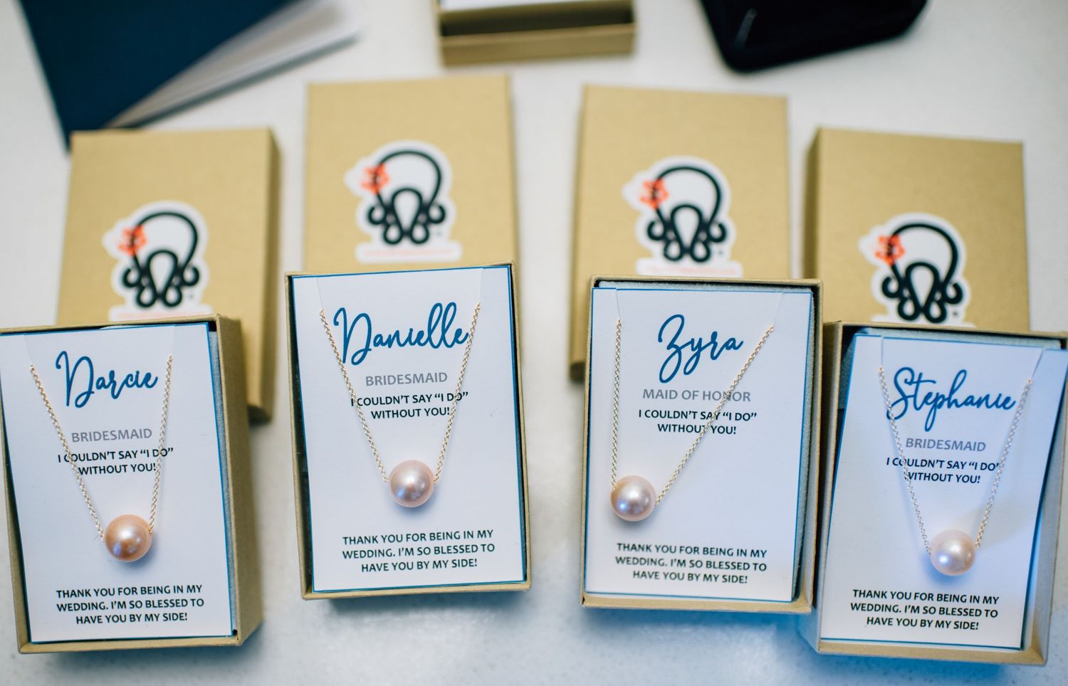 Four personalized wedding favor boxes with pearl accents and calligraphy names.