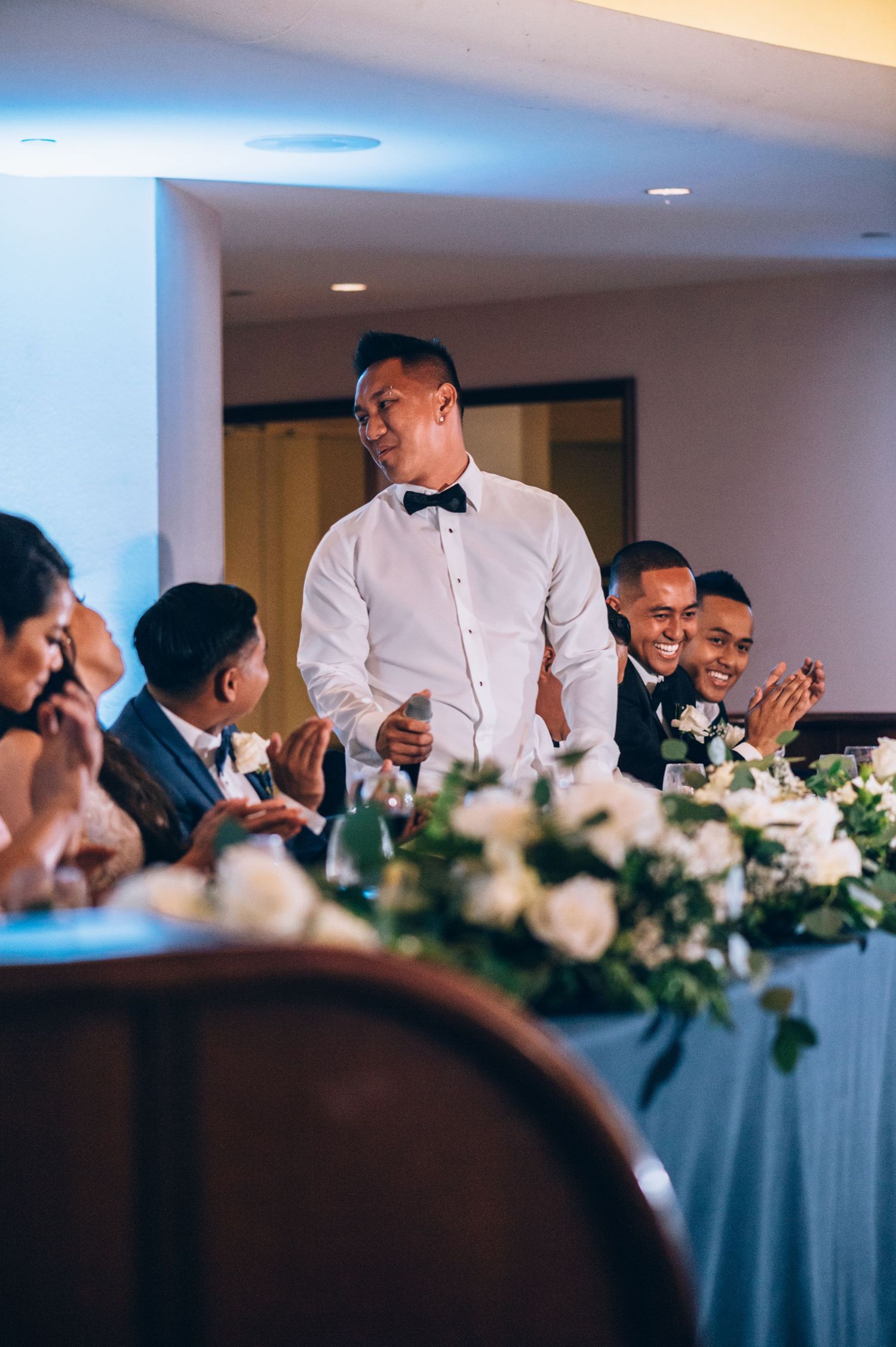 Guests enjoying a formal reception at a banquet table adorned with white floral centerpieces.