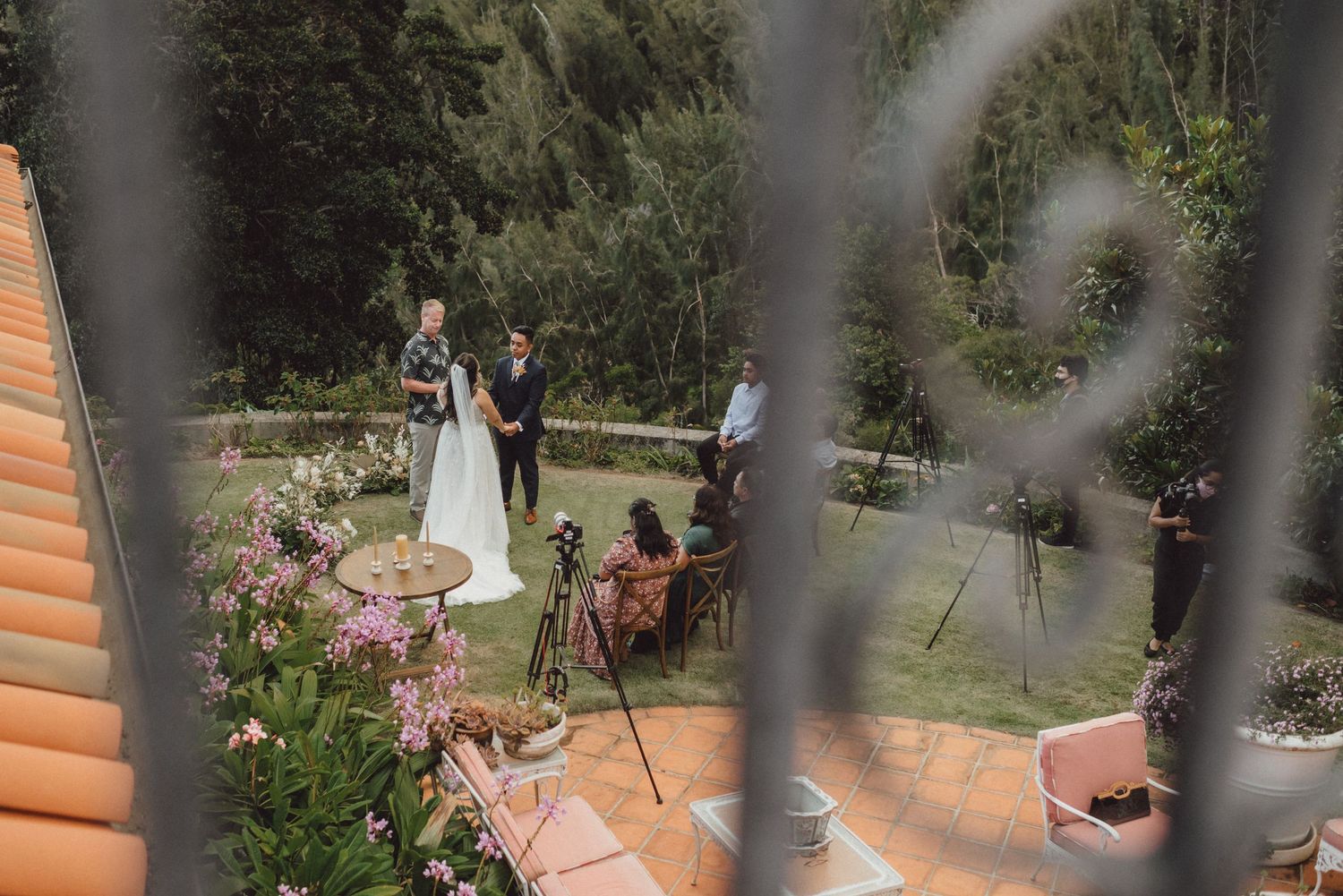 An intimate outdoor wedding ceremony viewed through decorative railings.