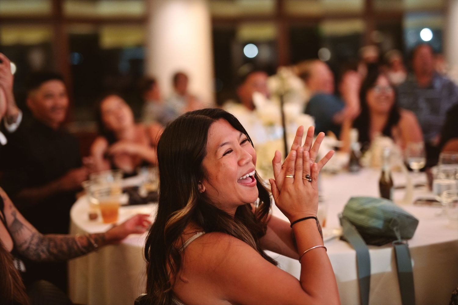 Woman laughing and clapping joyfully at an elegant indoor wedding reception dinner event.