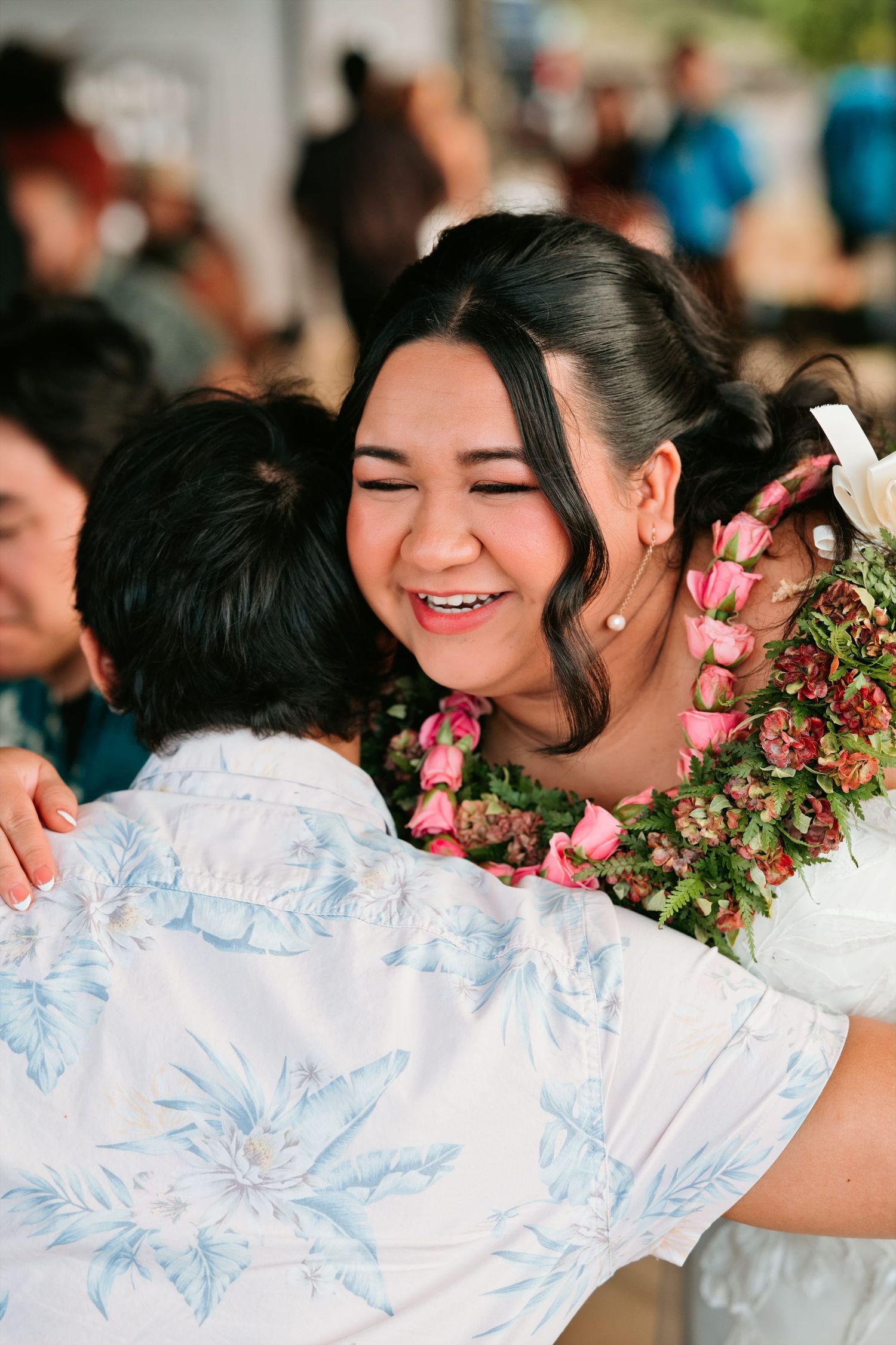 Smiling woman wearing floral lei receives warm hug at Hawaiian celebration event.