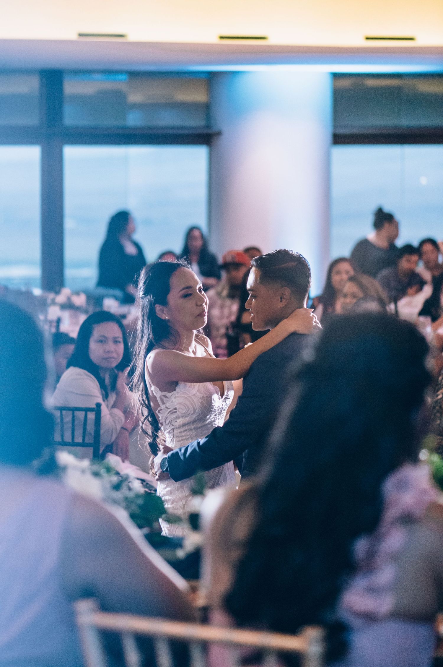 Wedding guests observe a romantic dance in a modern venue with blue-tinted lighting.
