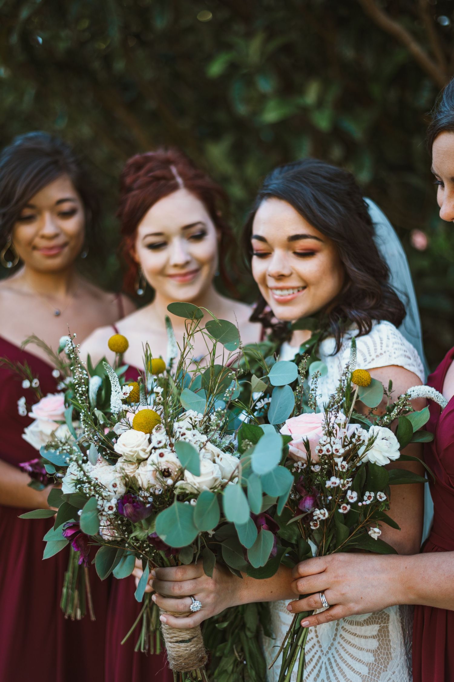 Bridesmaids in burgundy dresses hold matching white and green floral bouquets.