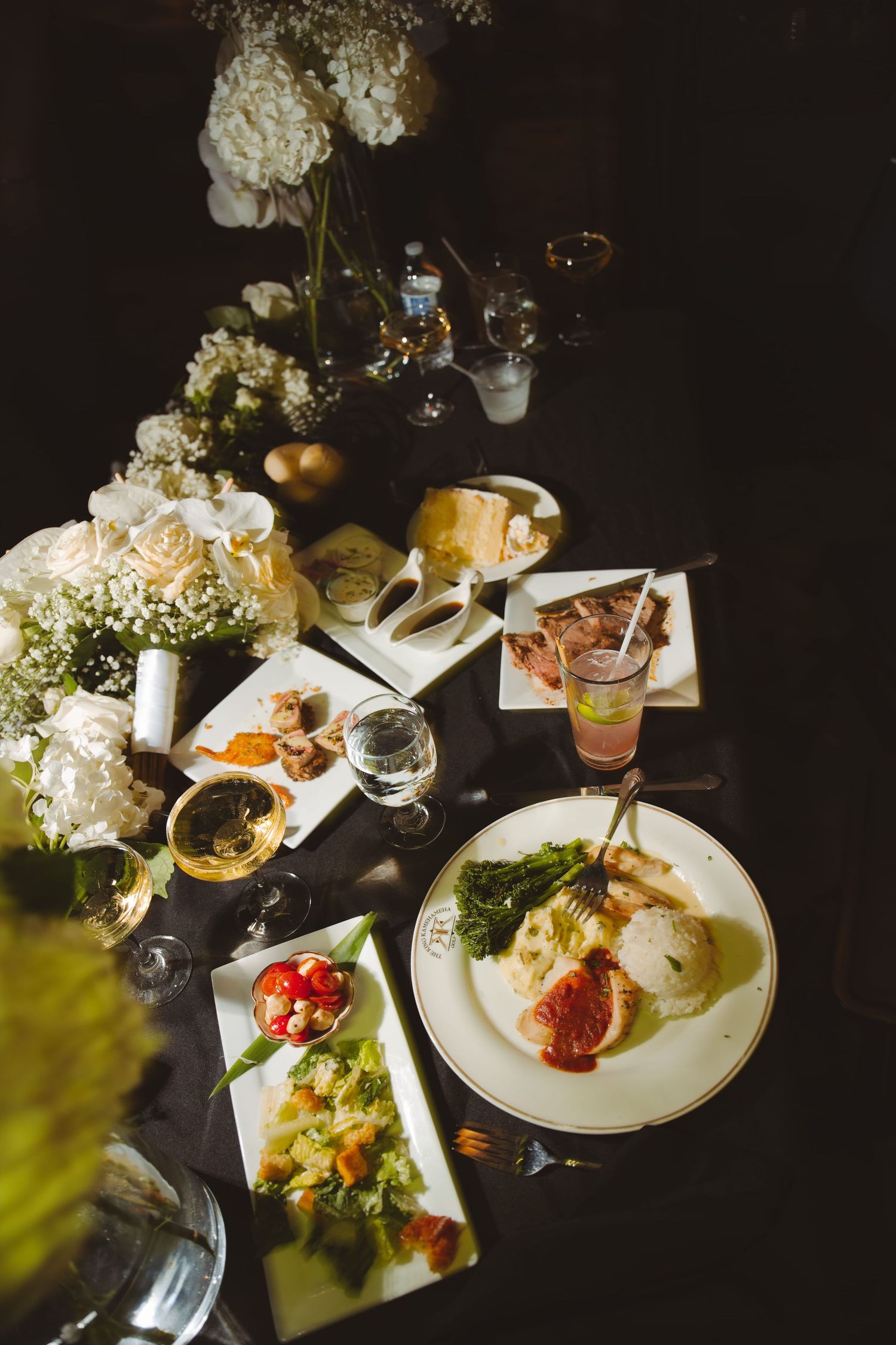 Elegant dinner table with white floral centerpieces, gourmet plated dishes, and glassware at a formal event.