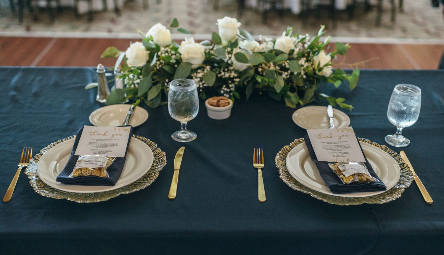 Elegant navy and gold wedding table setting with floral centerpieces and place cards.