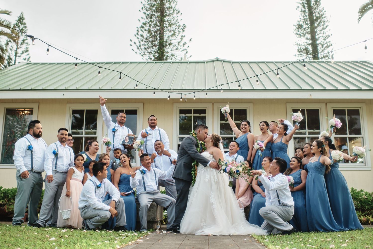 Wedding celebration group photo with attendees in blue and gray attire outside a building.