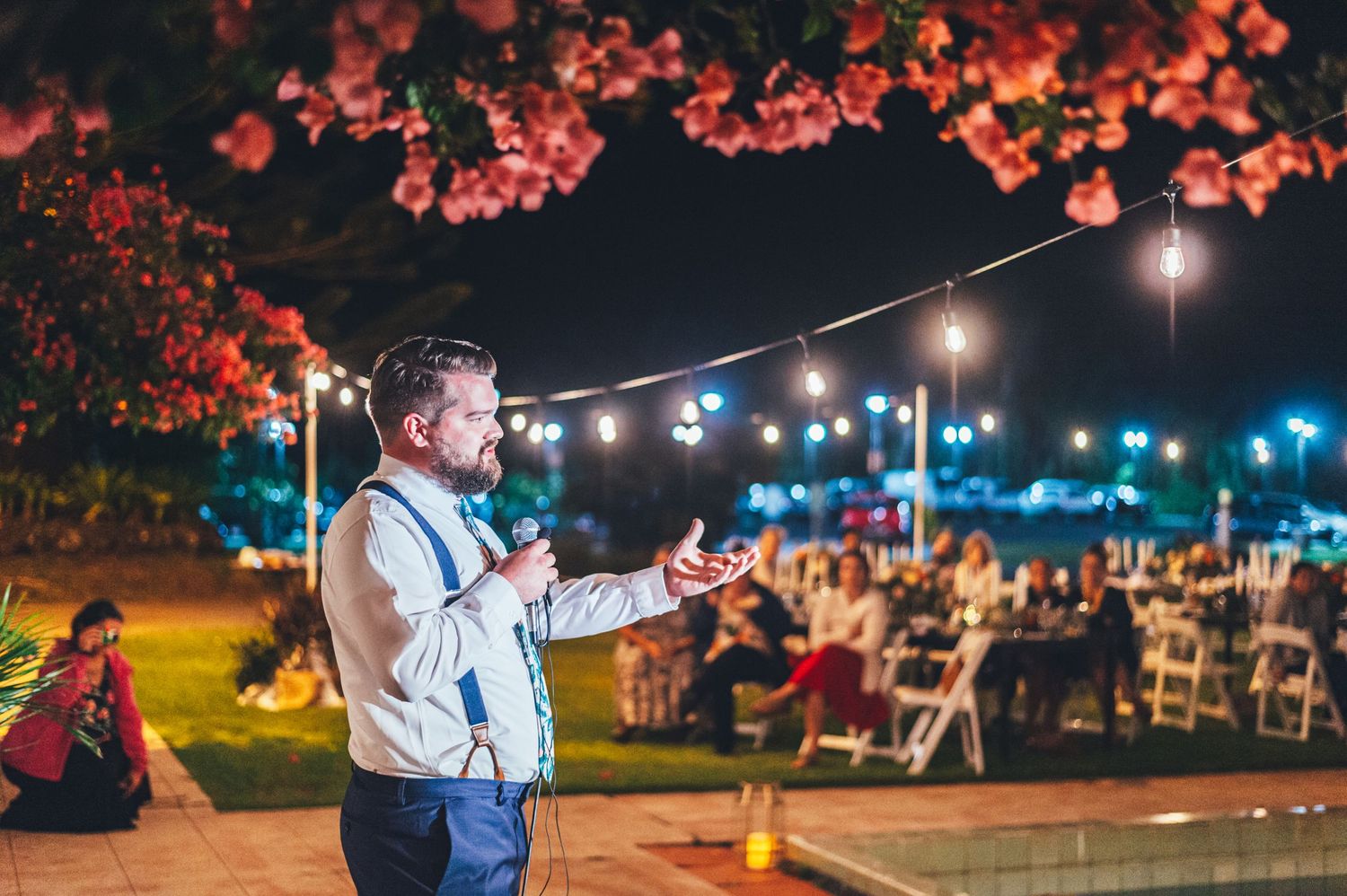 Outdoor evening wedding reception with string lights and red floral decorations.