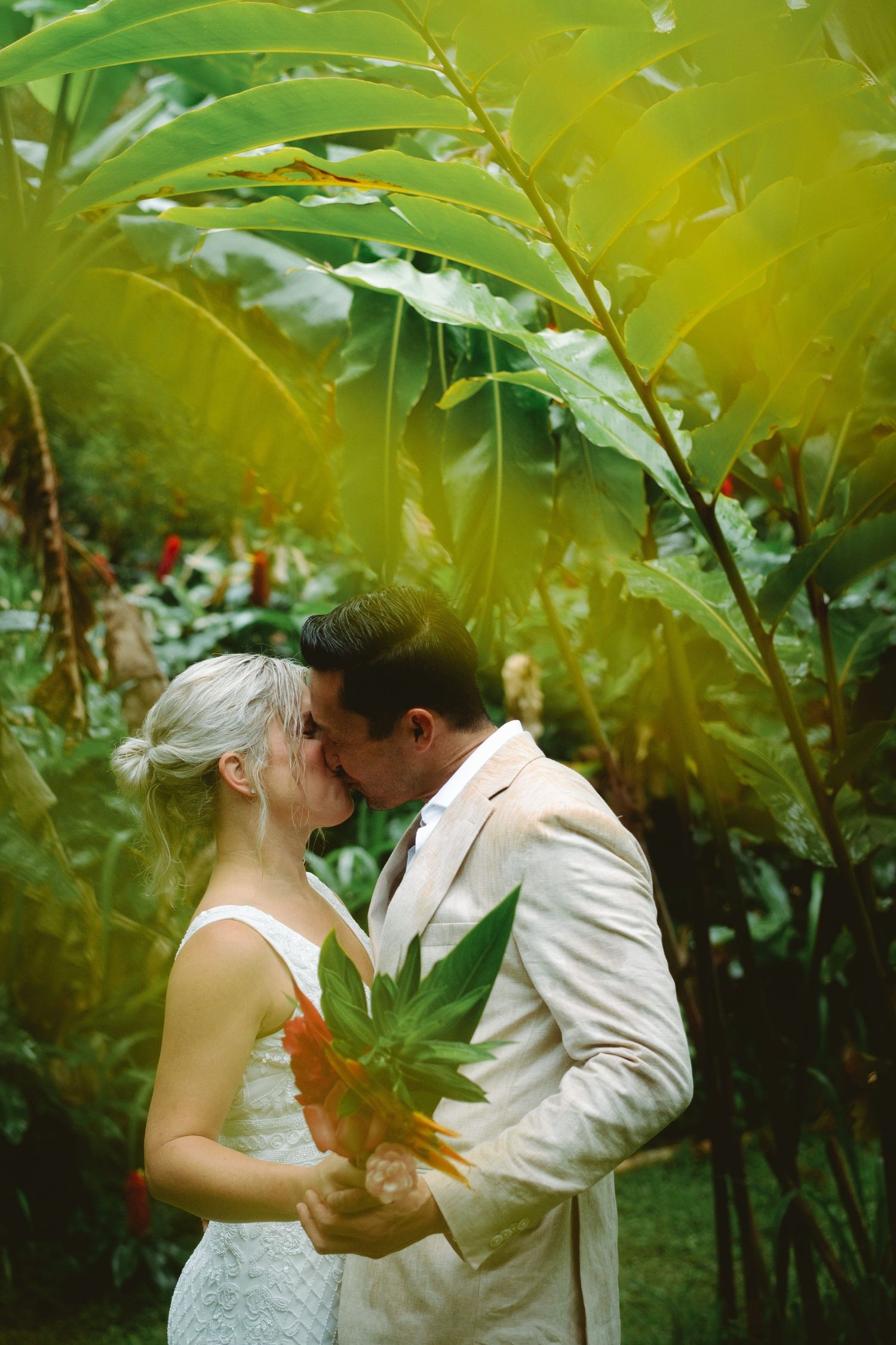 Bride and groom sharing a romantic kiss surrounded by lush tropical greenery.