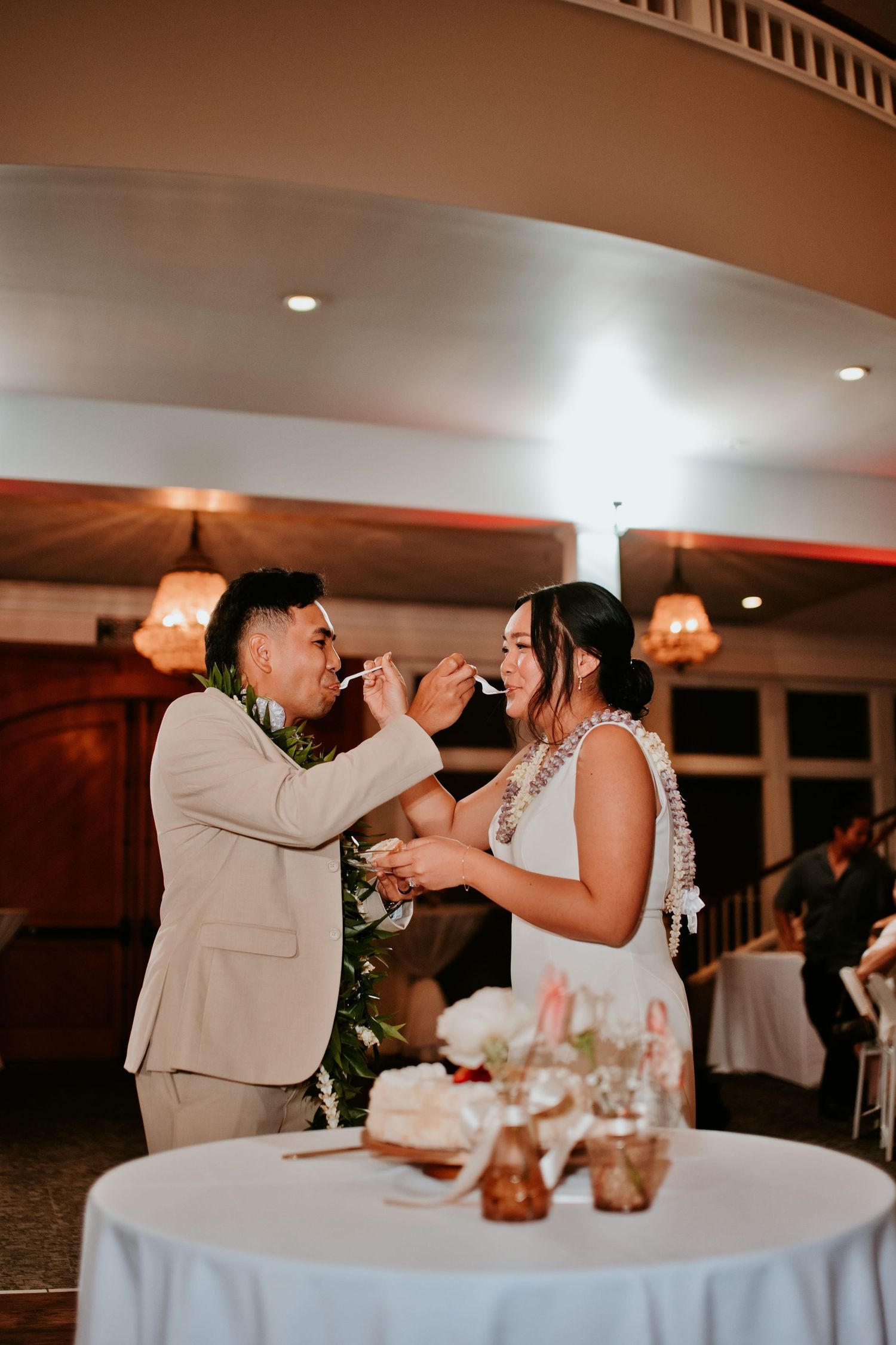 Bride and groom feeding each other wedding cake at elegant indoor reception venue.
