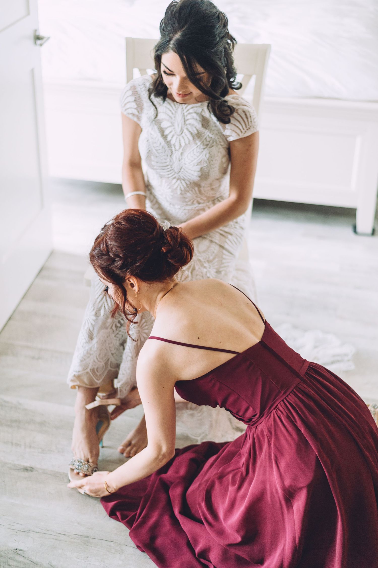 Two women in formal dresses prepare for a wedding event.