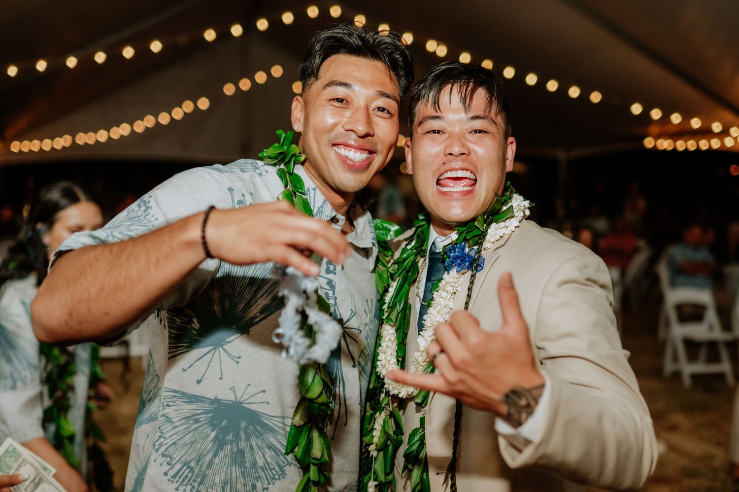 Joyful wedding celebration with dancers wearing green leis under string lights.
