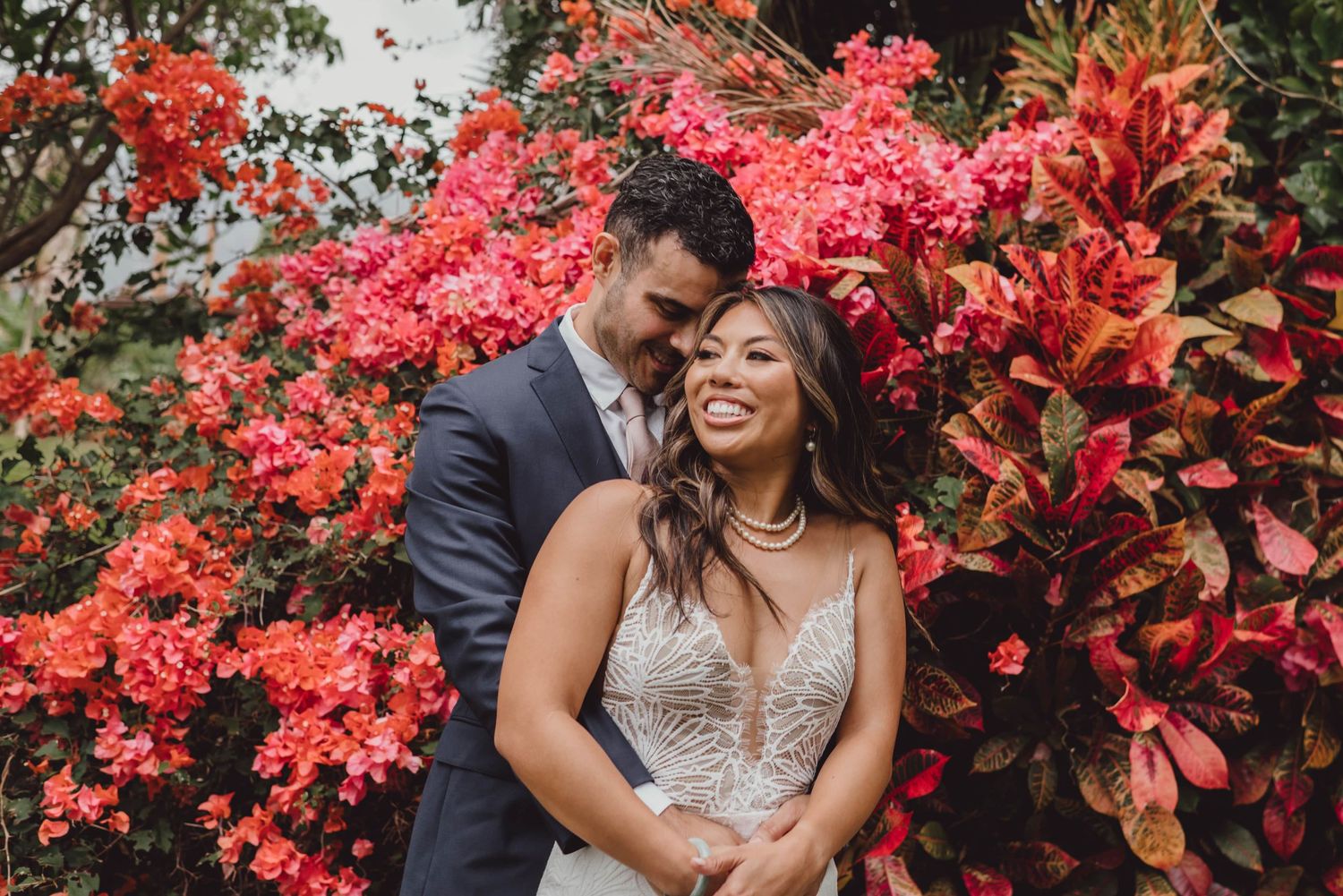 Groom embracing bride from behind in front of flowers at the Maui Tropical Plantation at Maui Wedding