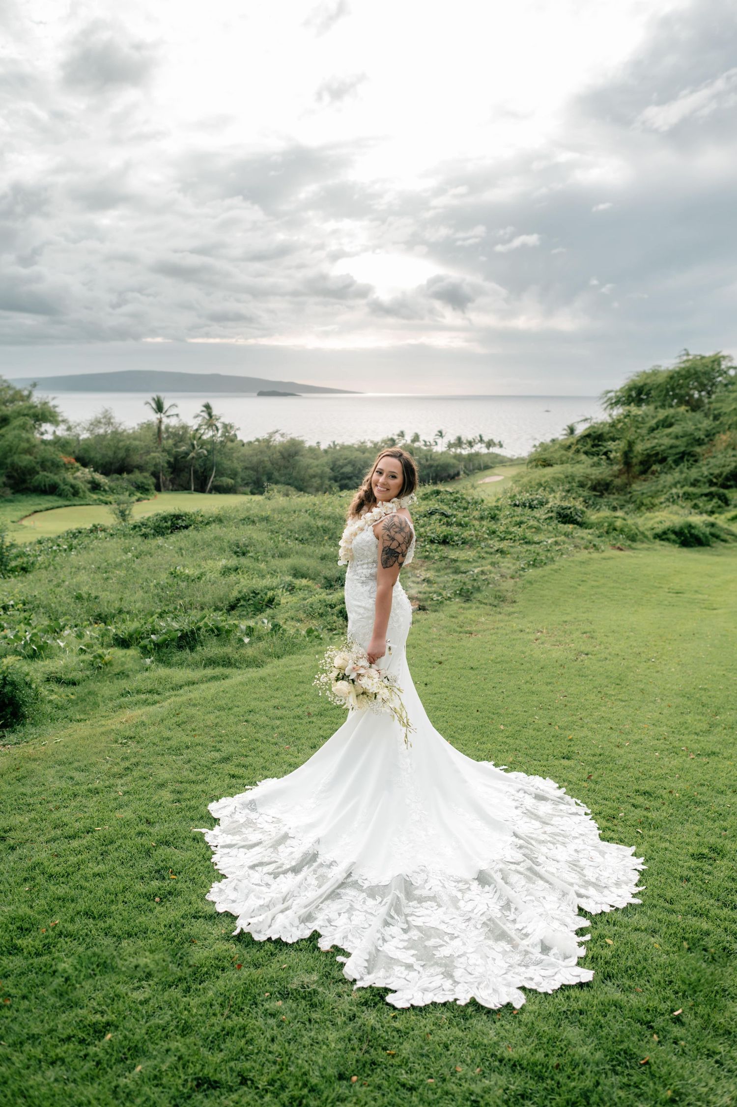 Stunning bridal gown with intricate lace train spreads across green hillside landscape.