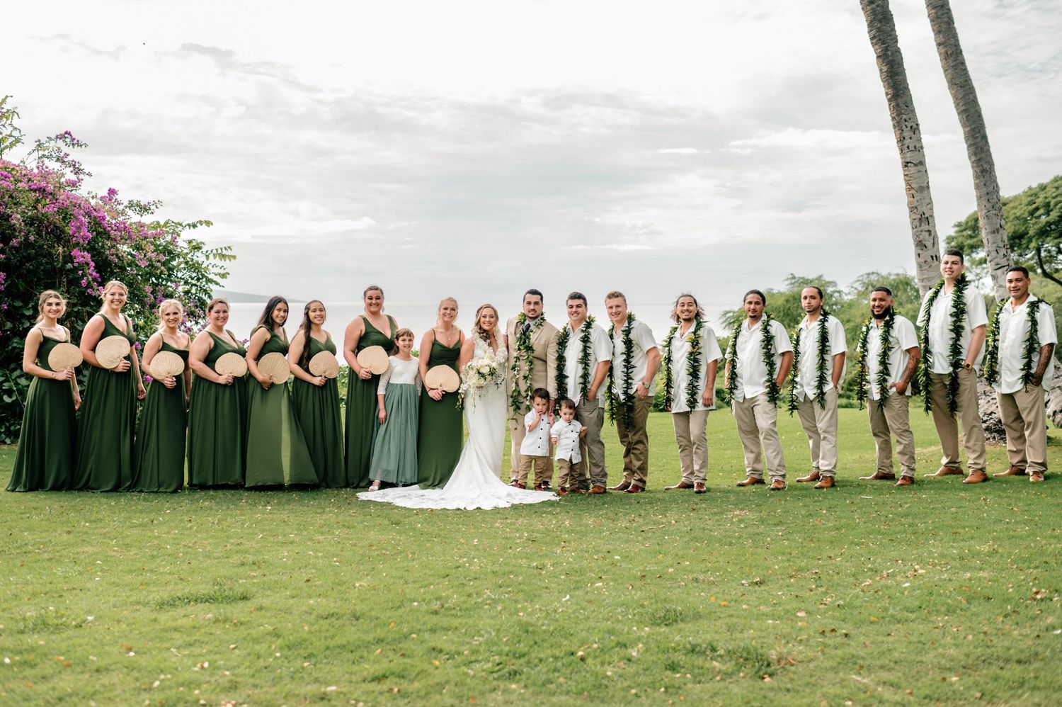 Full wedding party portrait with bridesmaids and groomsmen under palm trees.