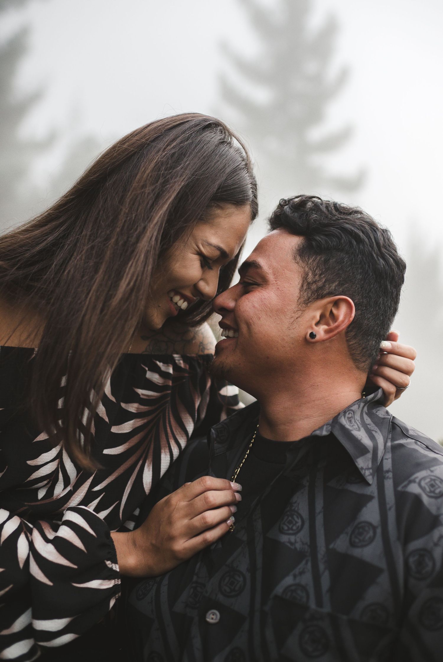 Couple shares intimate moments against a misty forest backdrop.