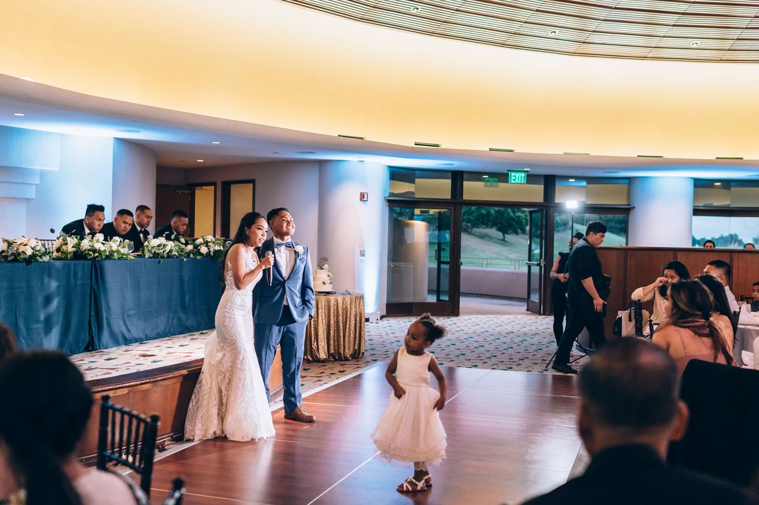 A couple shares their first dance at a wedding reception in an elegant ballroom with blue lighting.