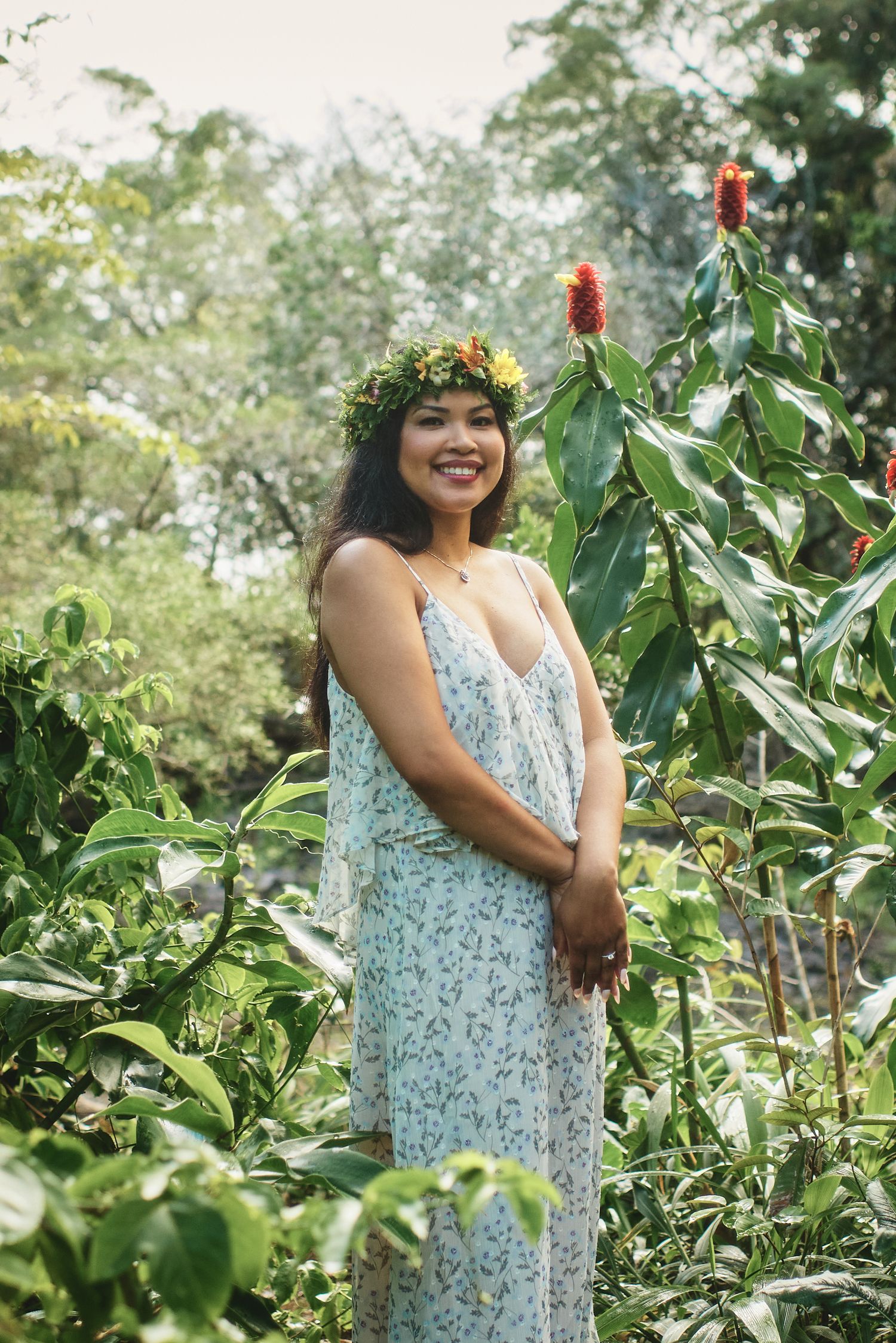 A person in a floral dress poses in a tropical garden wearing a flower crown.