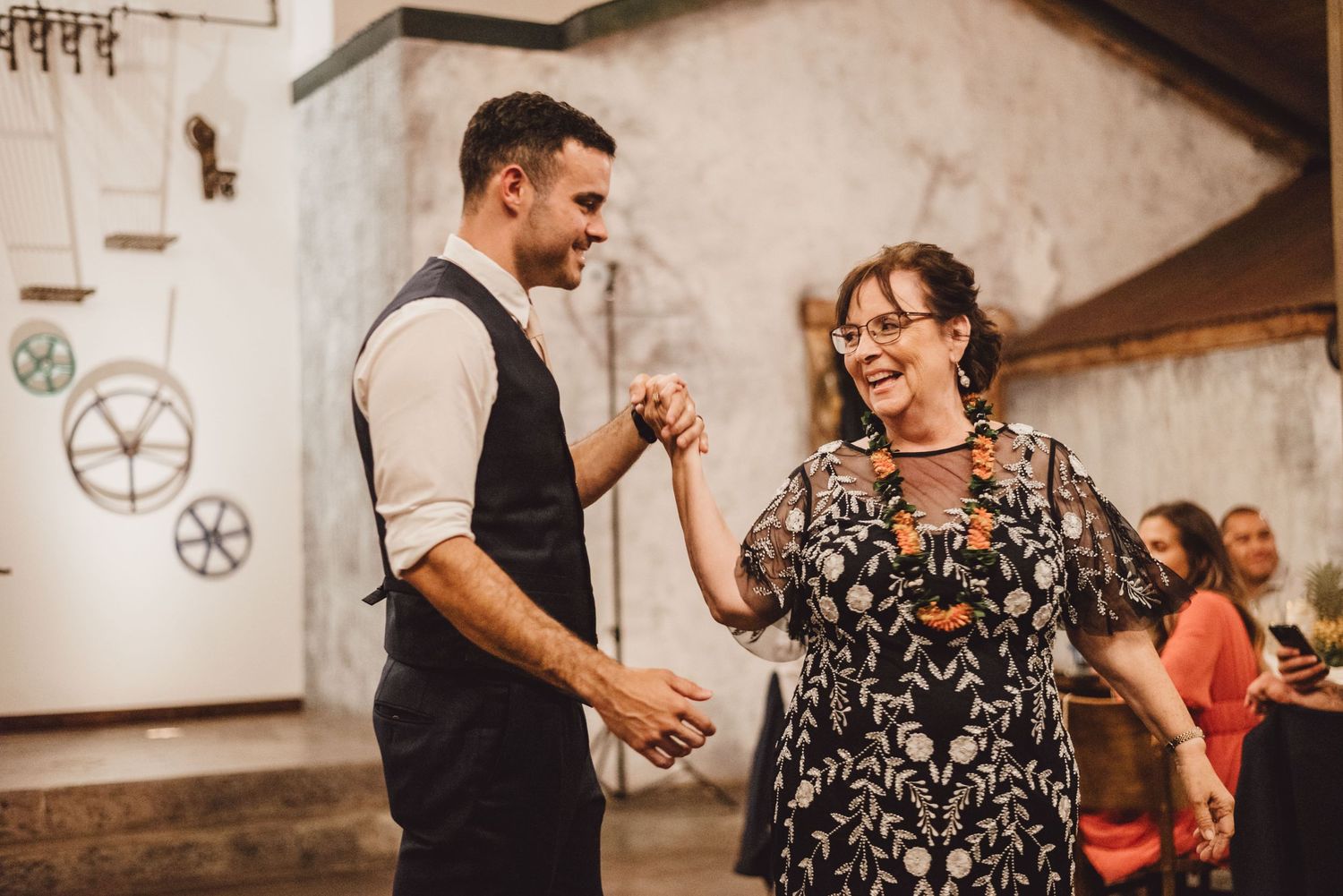 Guests dancing and celebrating at wedding reception in rustic venue with wooden walls.
