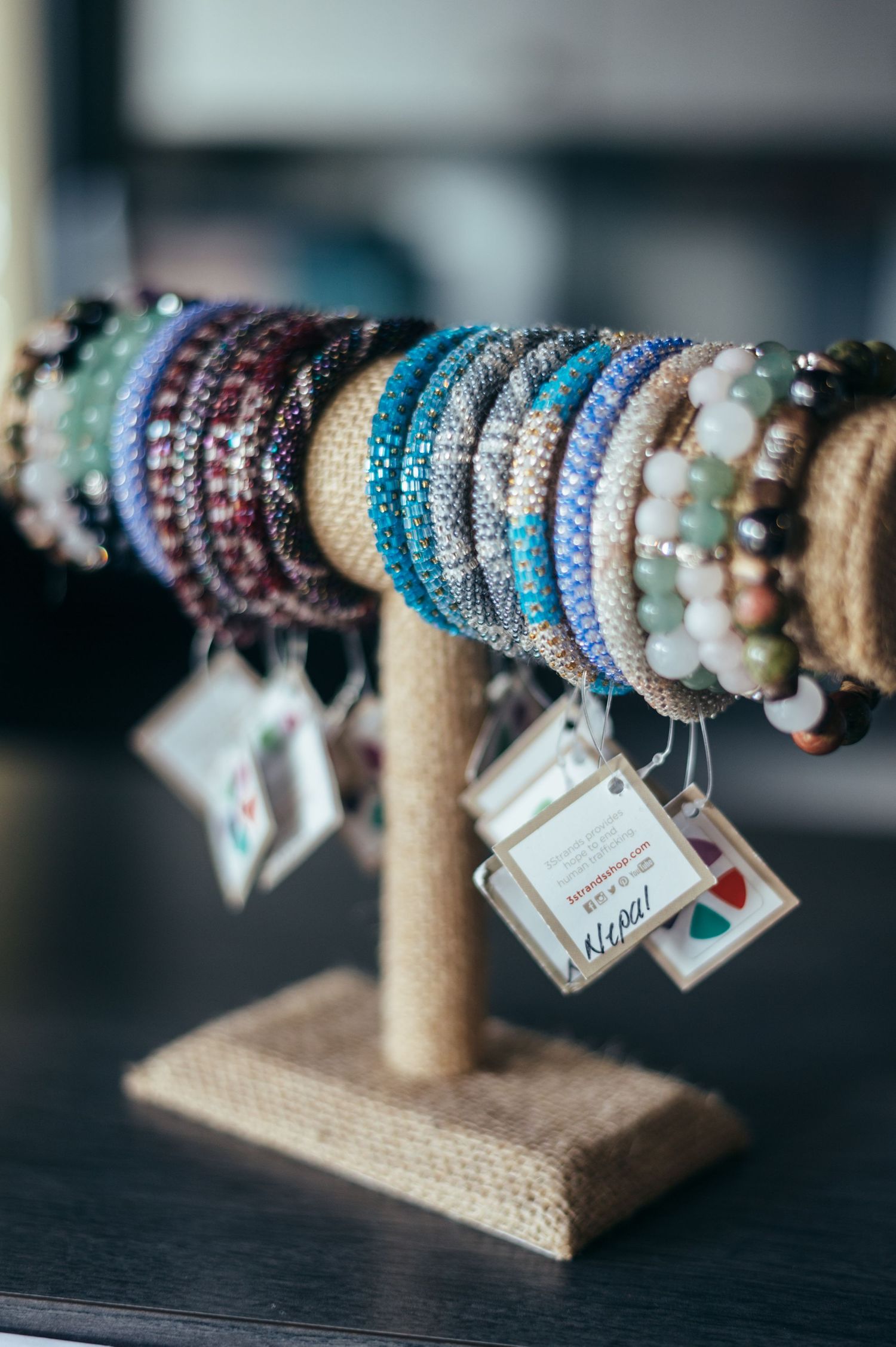 Colorful beaded bracelets displayed on a rustic burlap and wood jewelry stand.