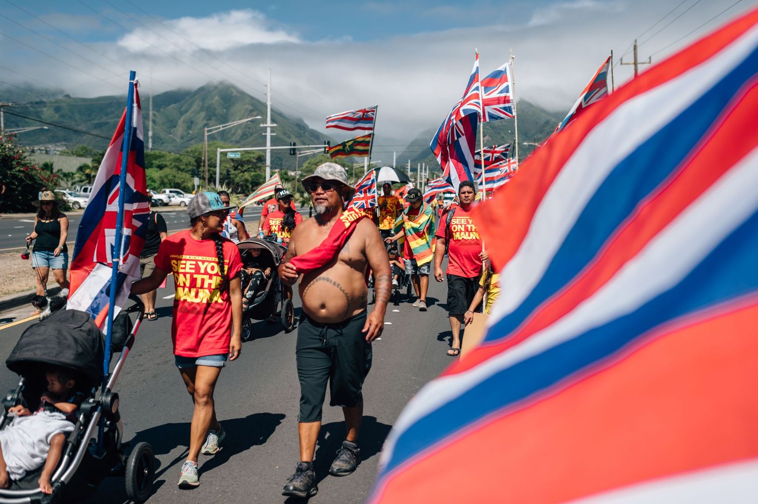 Hawaiian flags wave prominently as protesters march along street during demonstration.
