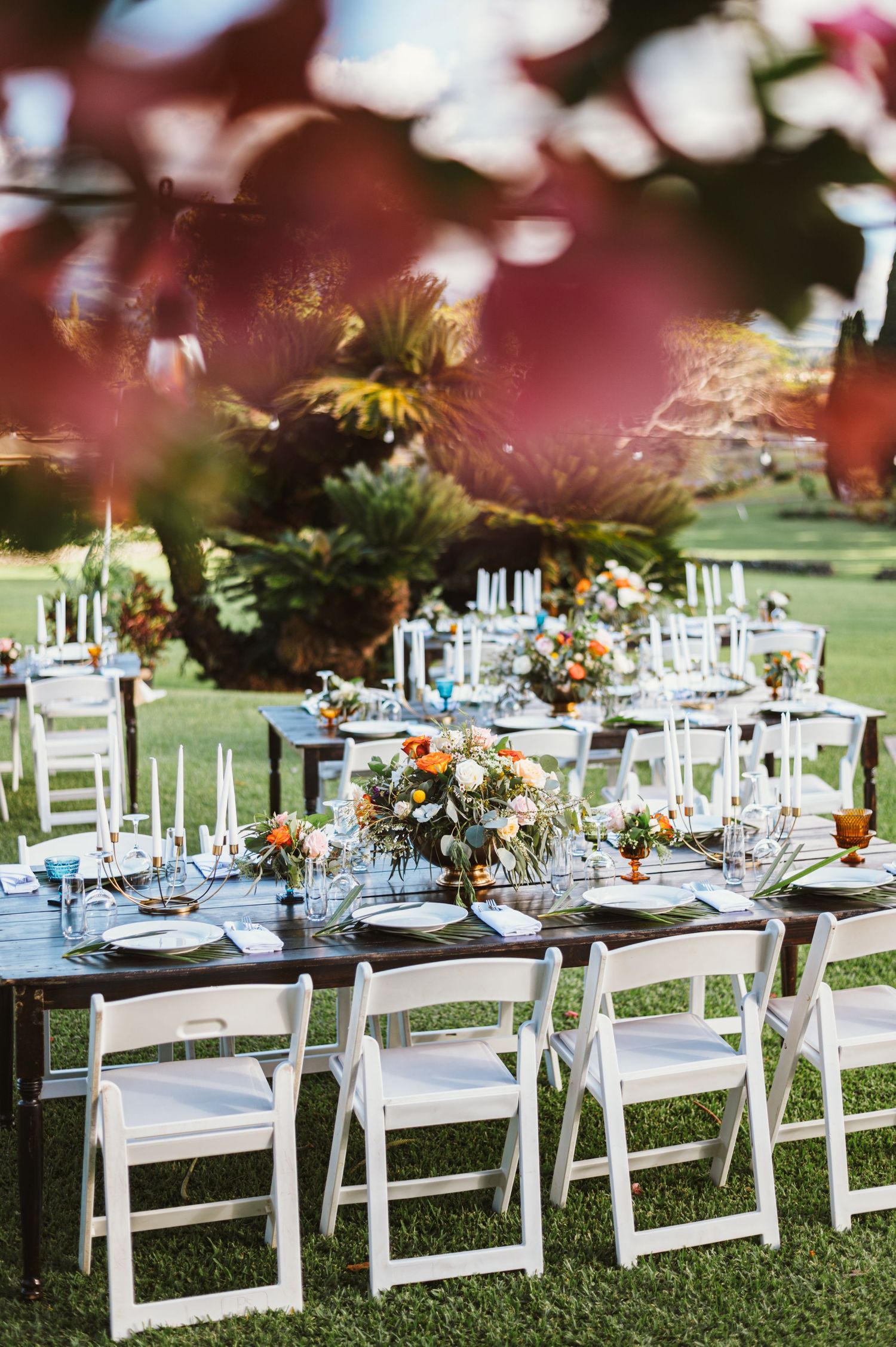 Elegant outdoor wedding reception setup with white chairs and floral centerpieces on grass.